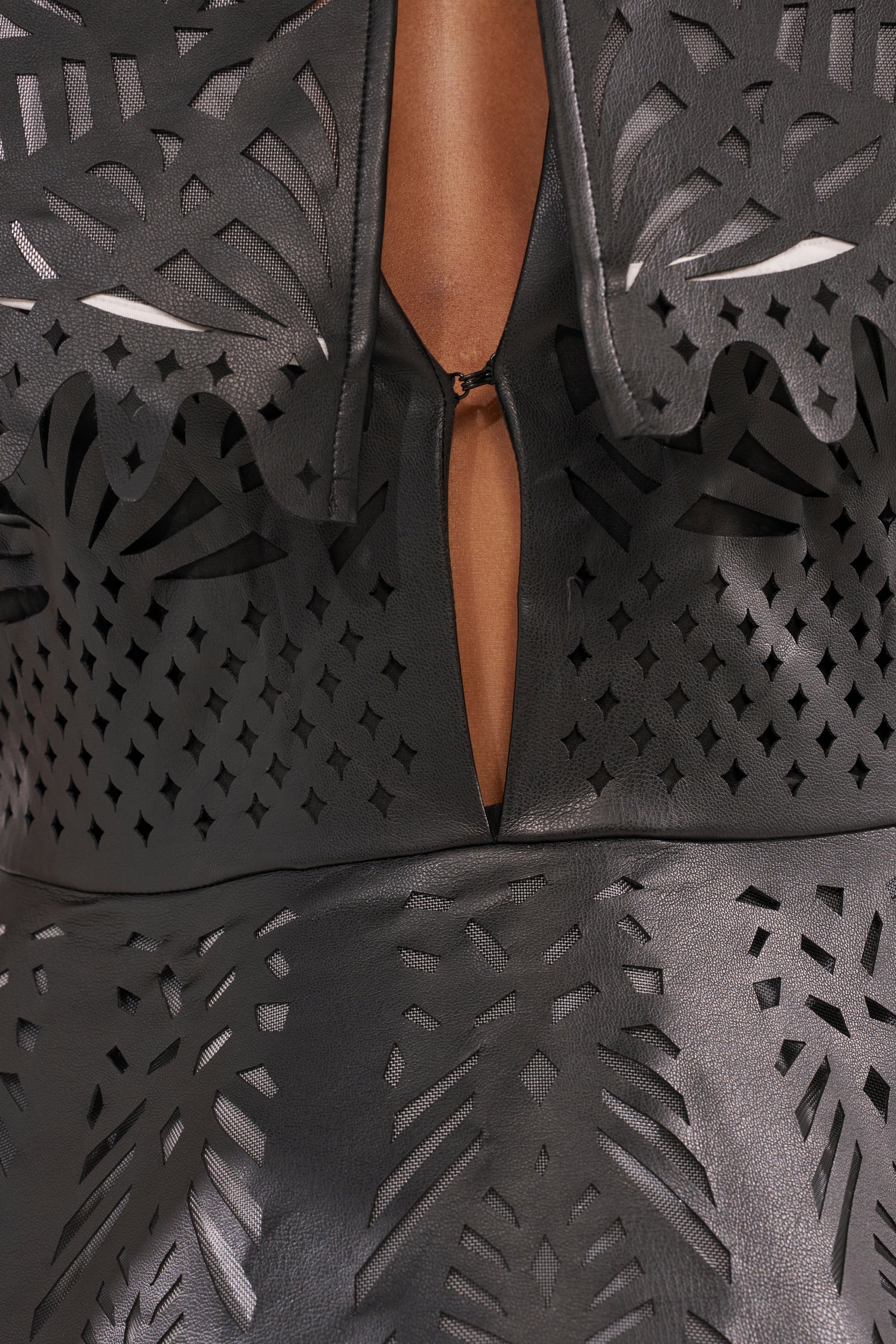 Close-up of the URBAN EDGE MINI COLLARED DRESS in black faux leather, featuring intricate laser-cut patterns and a front keyhole opening. Its glossy finish and bold design make it an ideal statement piece for cocktail parties. 7
