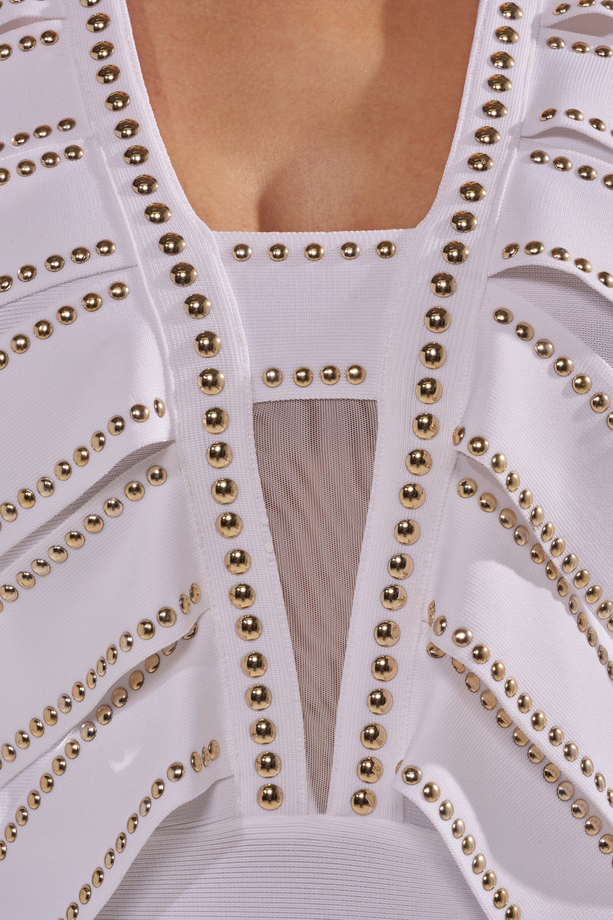Close-up of the ANGEL WINGS MINI DRESS, a white bodycon mini dress with gold stud accents and a bold chest cutout, revealing skin for a striking party-ready look. 7