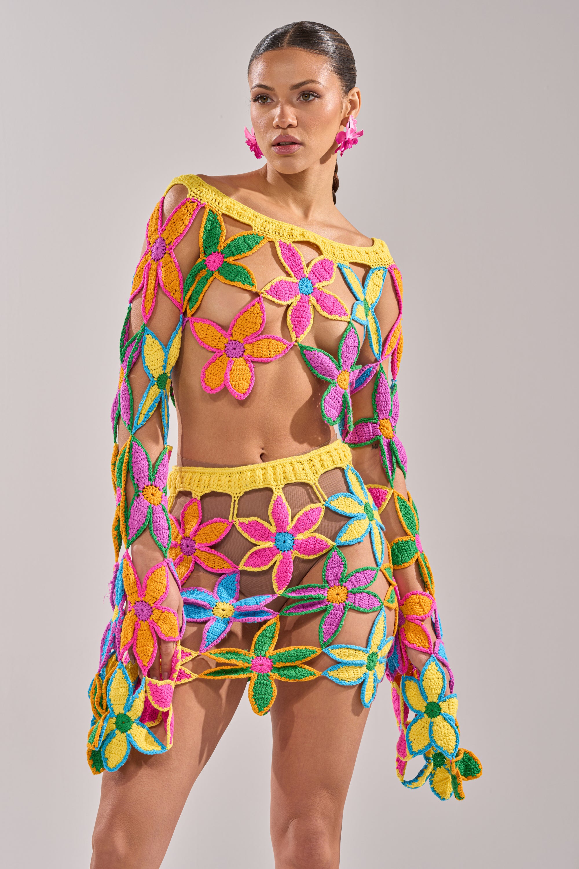 A woman poses in the FLORAL FIELDS CROCHET OFF THE SHOULDER SWEATER, a vibrant open-knit top with bold floral motifs in pink, yellow, green, and purple—perfect for summer parties with its playful and airy design. 4