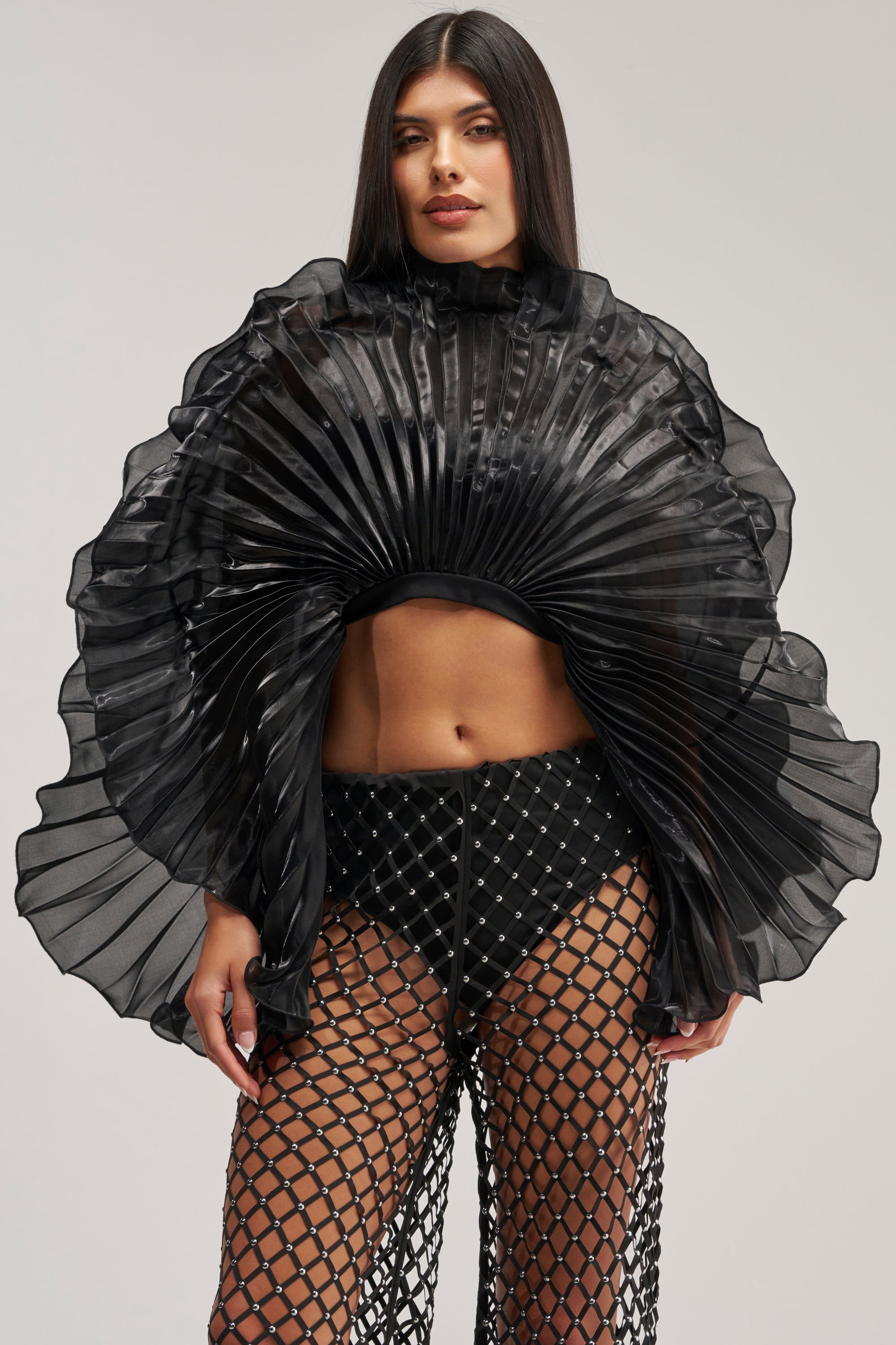 Model wears the SHINING DOWN ON YOU BLOUSE IN BLACK—a dramatic sheer pleated top with a striking ruffled circular motif—paired with black netted pants and undergarments, creating an avant garde look that's perfect for making bold evening statements.