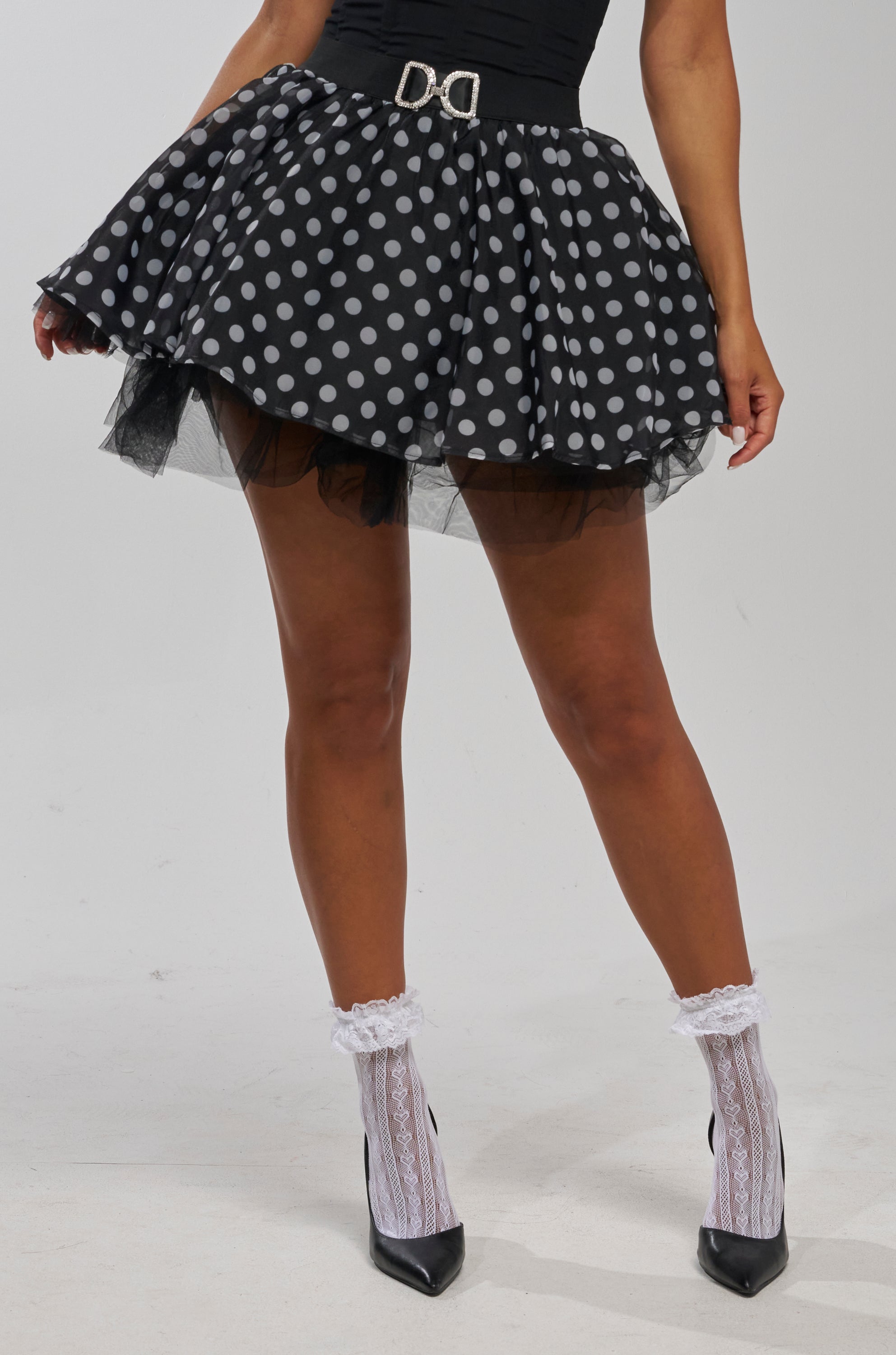 A person wearing the EXTREME MESH MINI SKIRT IN POLKA DOT, a black top, white lace socks, and black heels. The image is cropped to show only their body from the waist down.