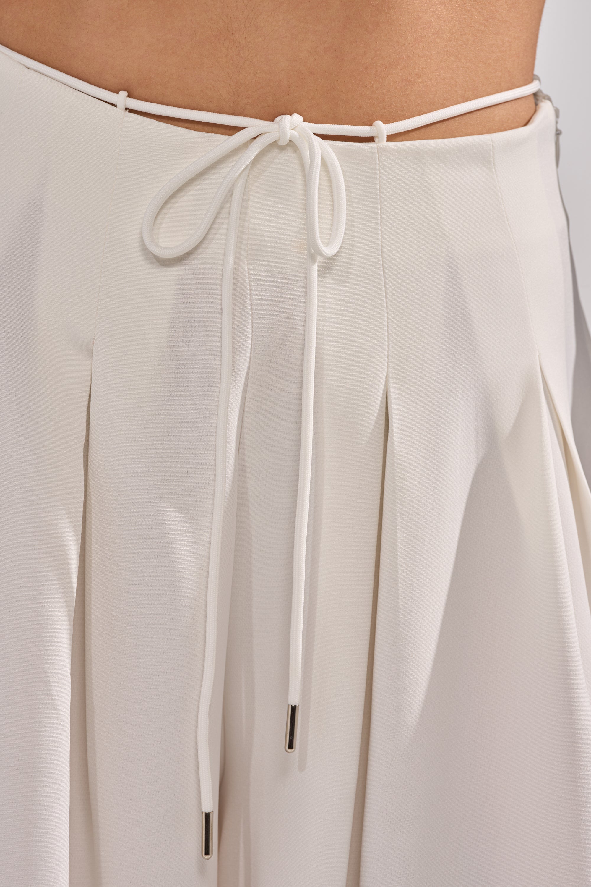 Close-up of the GLORIOUS PLEATED WIDE LEG TROUSER in white, featuring soft, flowing pleats and a thin waistband tie with a neat front bow—a versatile essential for an elegant touch.