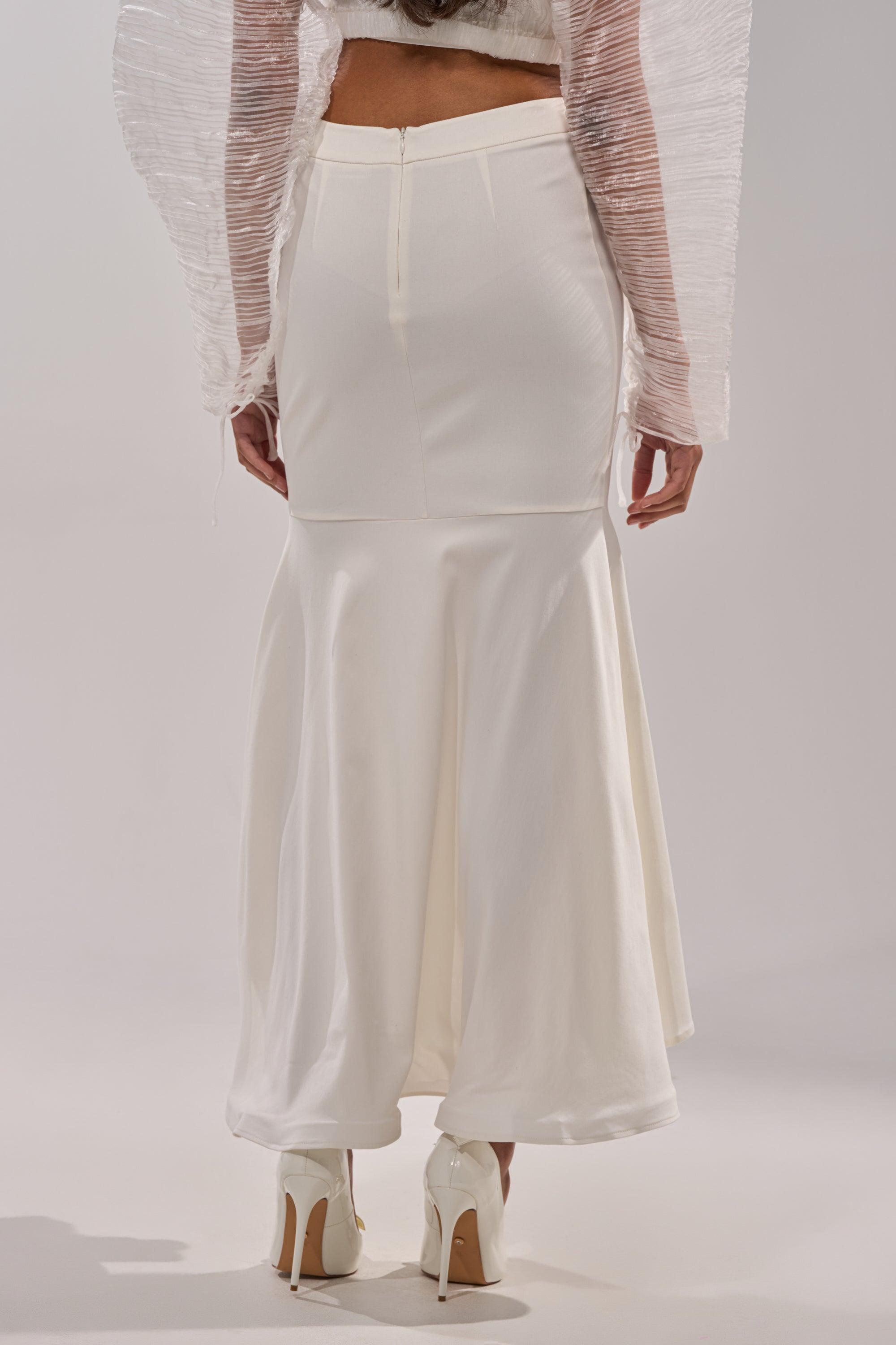 A person is shown from the back in a LEMON SATIN MAXI SKIRT, paired with a sheer textured long-sleeve top and white high-heeled shoes, all set against a plain background. 4
