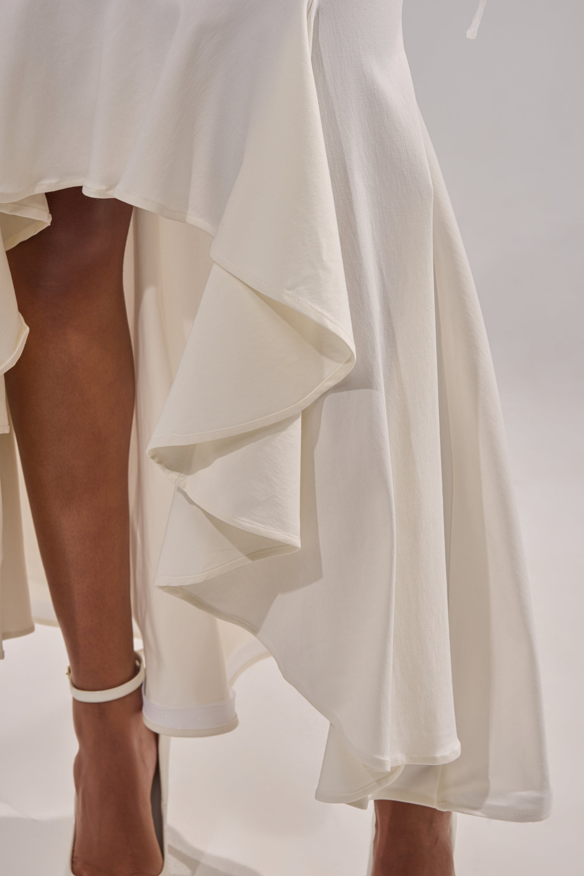 Close-up of a person wearing the LEMON SATIN MAXI SKIRT, styled with white ankle-strap heels, standing against a neutral background. 6