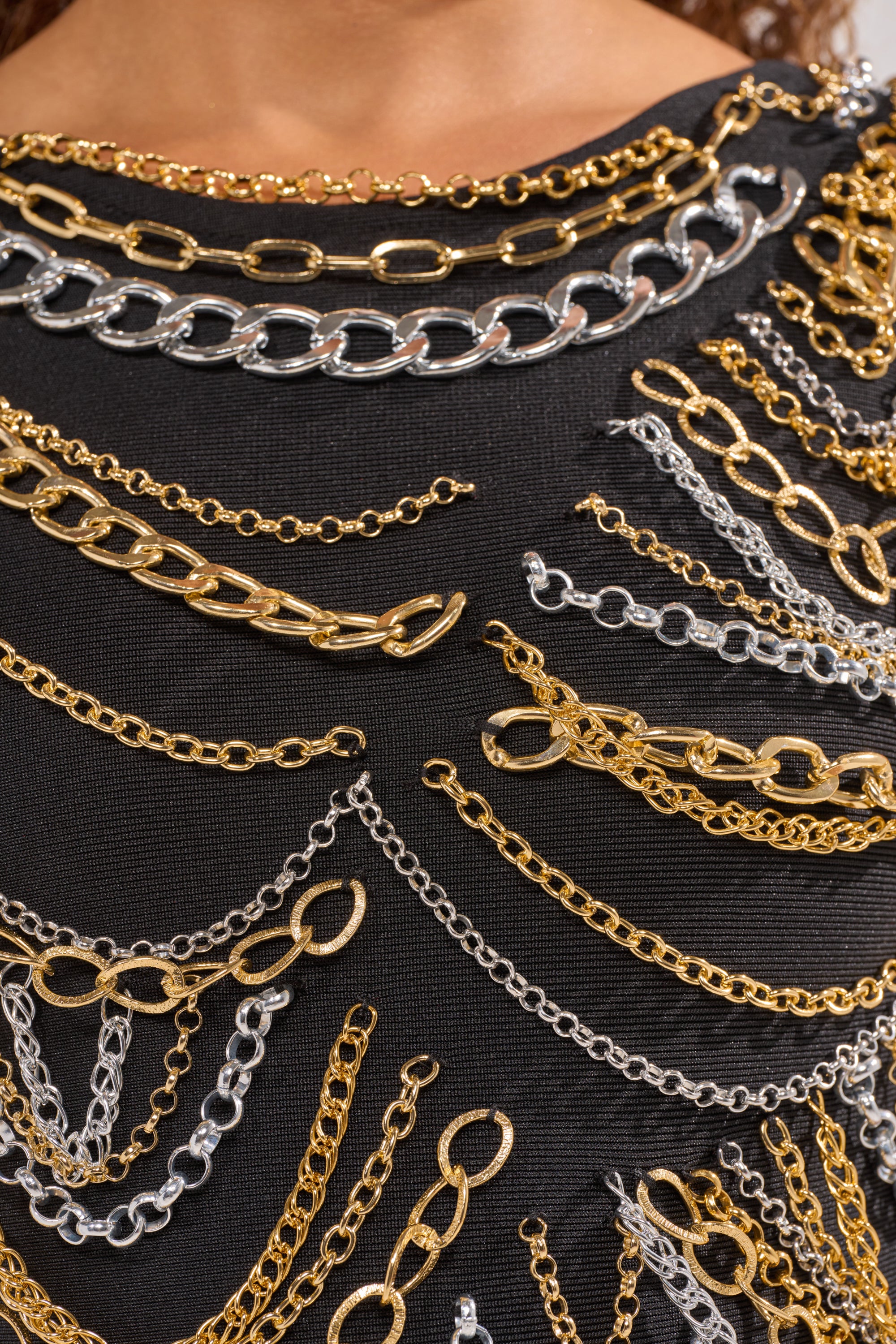 A close-up of the BLOWING KISSES CHAIN DETAIL MINI DRESS, a black bandage mini dress embellished with layered gold and silver chains—a show-stopping festival outfit. 6