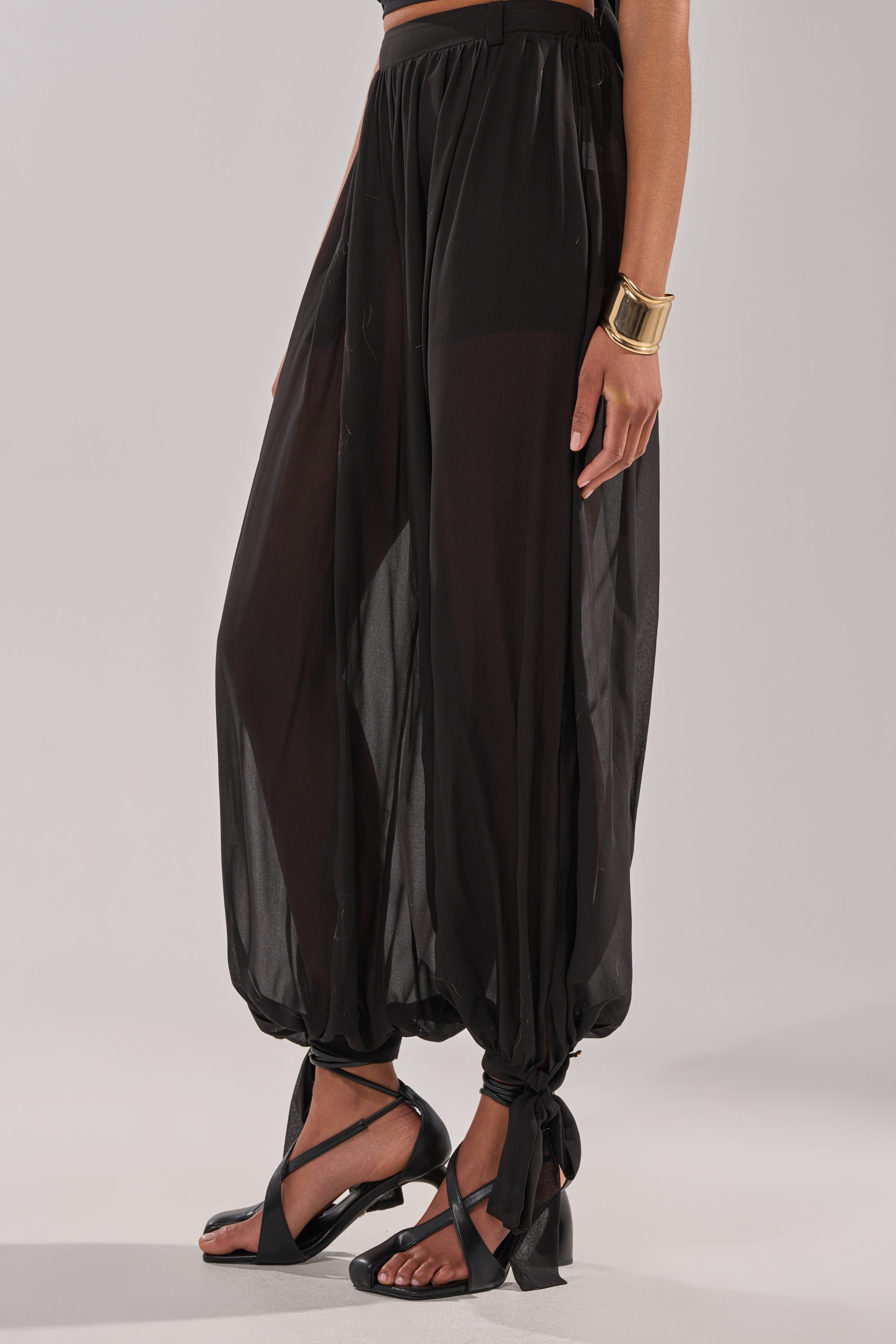 Wearing TRENDY BALLON PANT tied at the ankles, black open-toe sandals, a gold cuff bracelet, and a black crop top, this person stands against a neutral background. 6