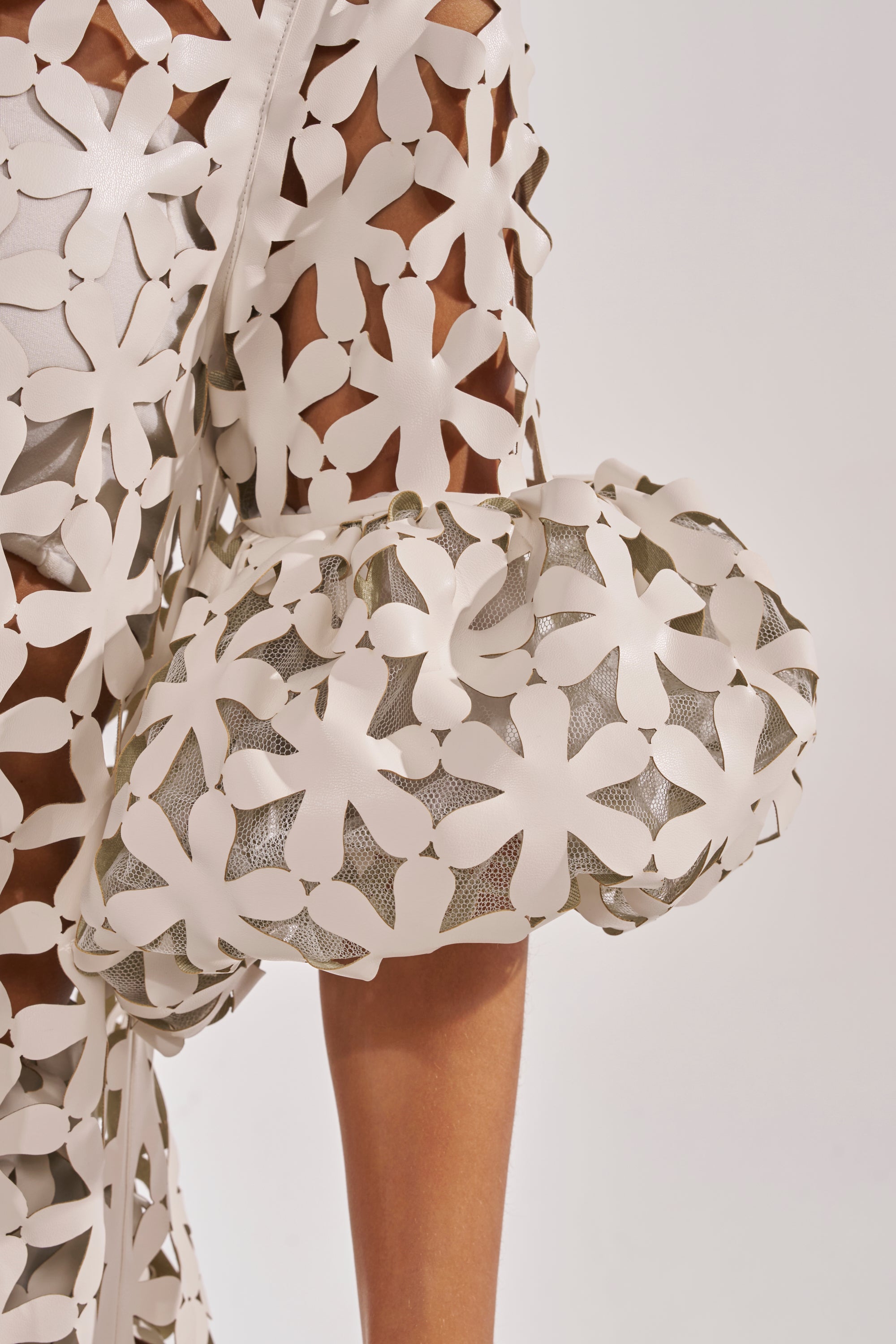 Close-up of the LEAH DUSTER, a white garment featuring puffy sleeves and cut-out floral lattice details over sheer mesh, creating a textured and airy look perfect for chic resort wear. 7