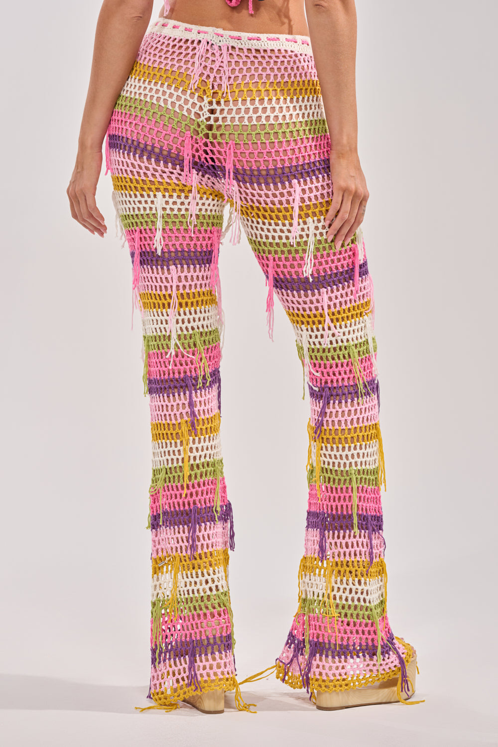 A person wears the RESORT BABE CROCHET PANT, featuring colorful pink, yellow, orange, and purple crochet with fringe details, photographed from the back against a plain light background—a bold boho festival look. 3