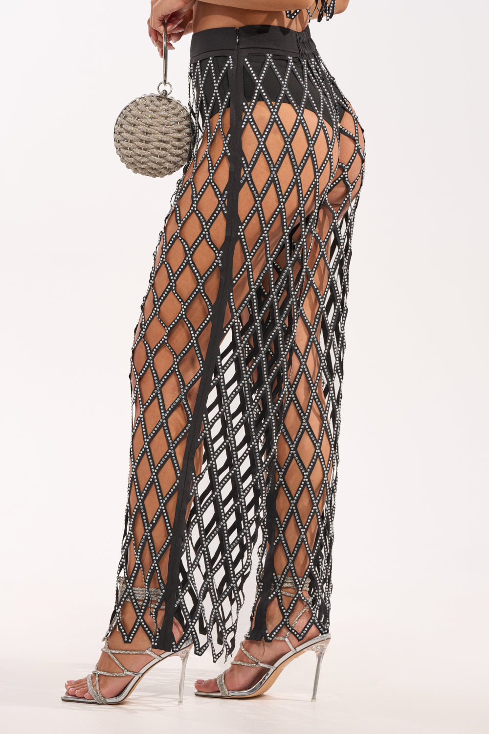 A person wearing the ROCK N ROLL RHINESTONE TROUSER featuring a diamond-shaped black net overlay, styled with a round silver purse and high-heeled sandals. 5