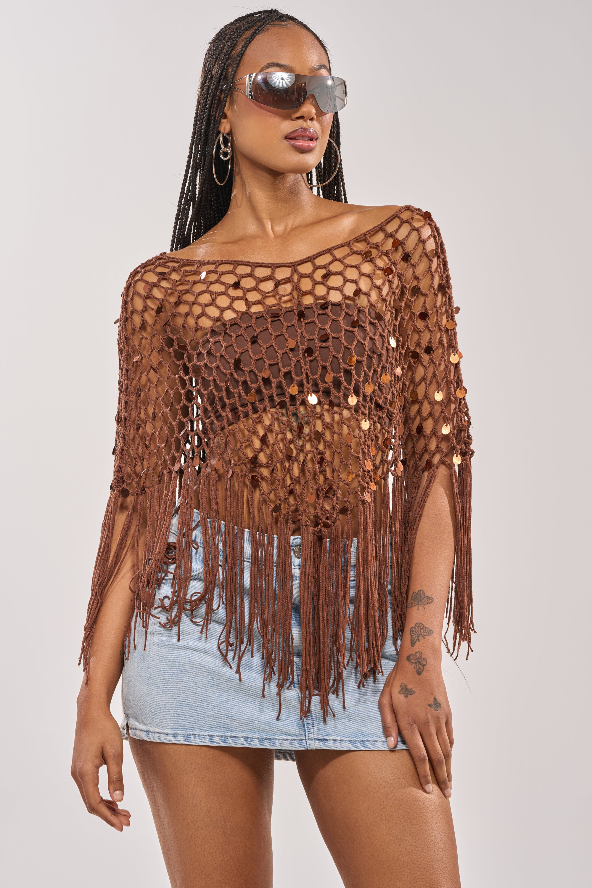 Woman wearing SHAKE IT QUEEN CROCHET BLOUSE with metallic accents over a brown bra, light blue denim mini skirt, sunglasses, hoop earrings. She has braided hair and visible tattoos on her left hand. 3