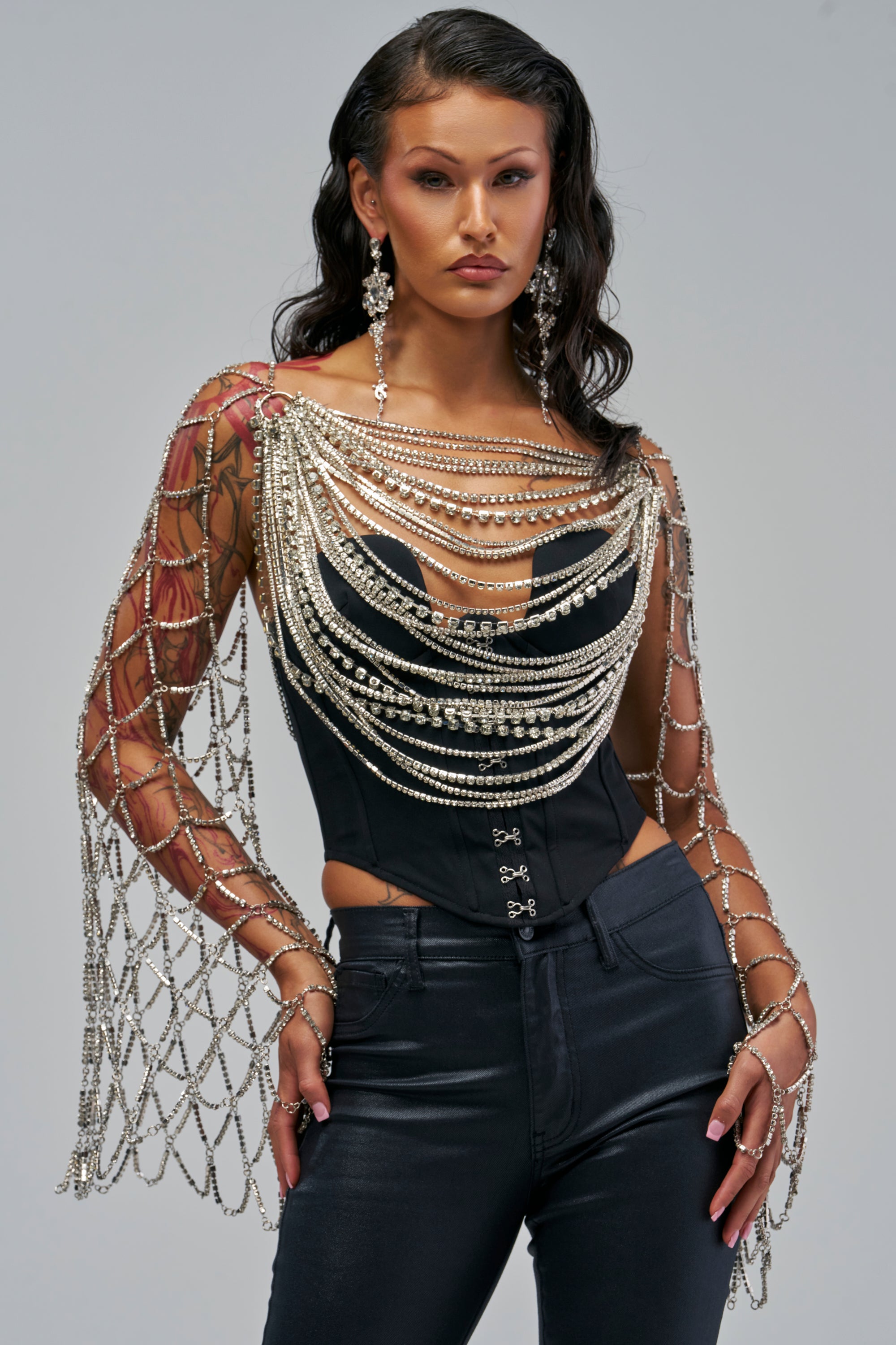 The DROPPED CHAIN ILLUSION TOP is a black corset featuring a draped, silver rhinestone chainmail overlay that extends over the shoulders and down the arms as a net-like sleeve.