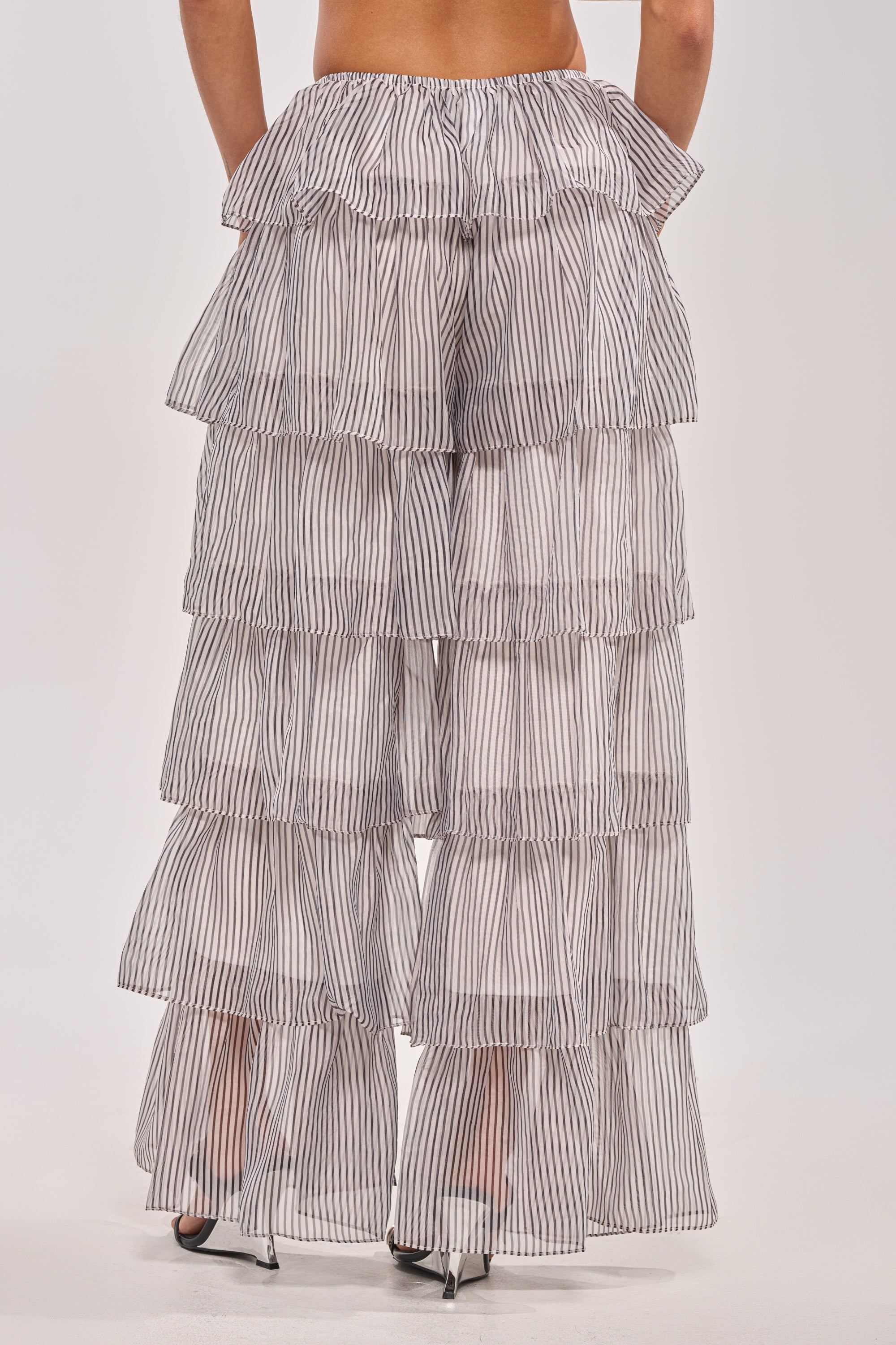 A person models the ALL I WANT TO DO STRIPE PALAZZO PANT—ruffled, with black vertical stripes, shown waist down against a plain backdrop—ideal for a chic spring festival look. 3