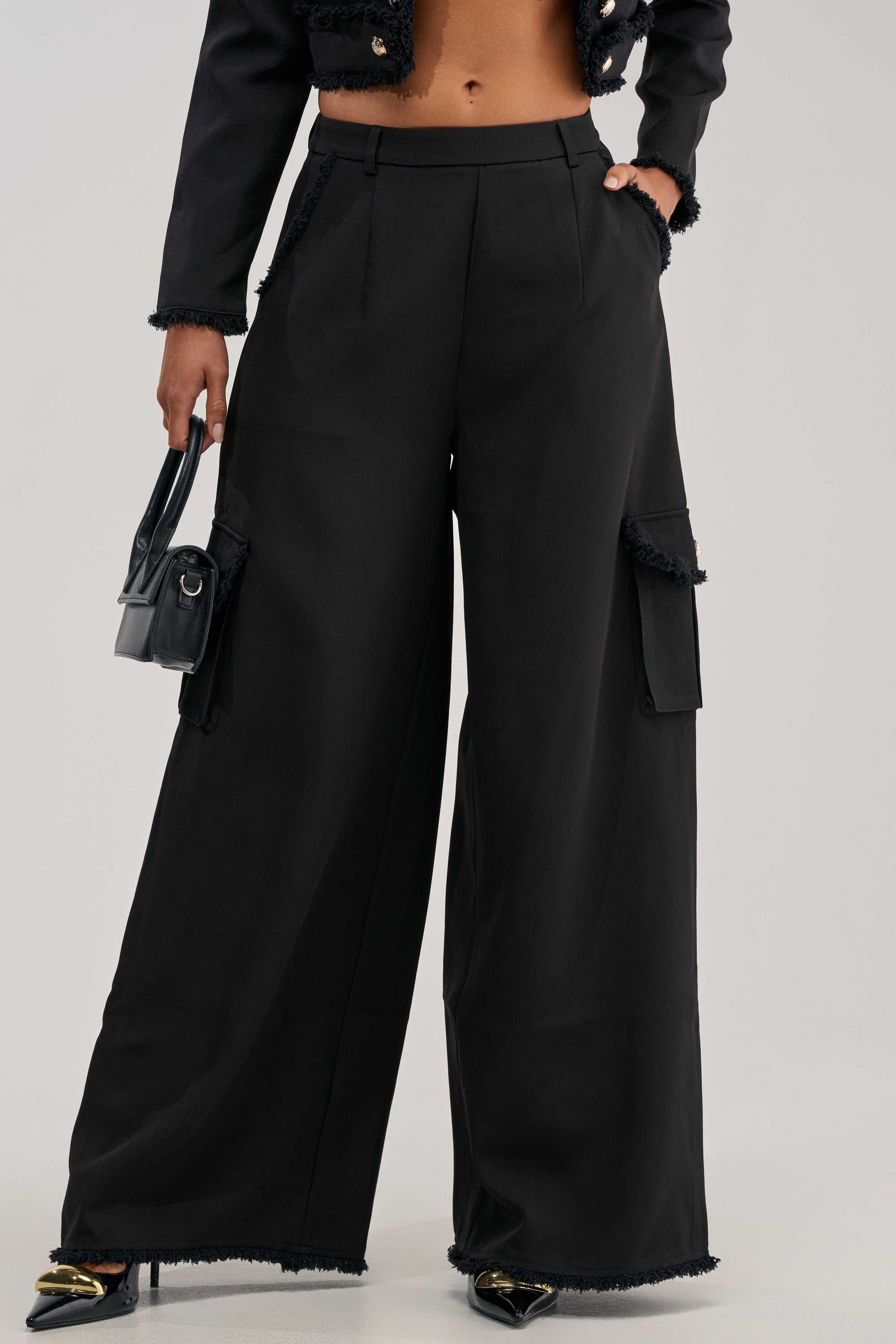 Wearing the CLASSY VIBE CARGO TROUSER—high-waisted, wide-leg black pants with pockets—paired with a matching black jacket, a small black handbag, and black pointed-toe shoes creates an effortlessly chic office wear look that highlights the elegance of a wide-leg silhouette.