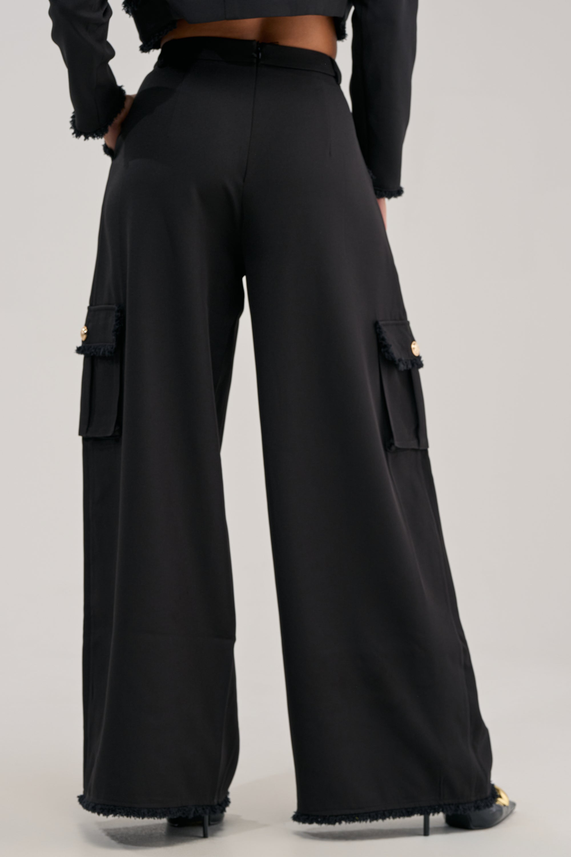 Model showcasing the CLASSY VIBE CARGO TROUSER—high-waisted, wide-leg cargo trousers featuring large side pockets—paired with black shoes. The shot focuses on the lower half of the body against a plain background, emphasizing the contemporary wide-leg silhouette that’s perfect for modern office wear.