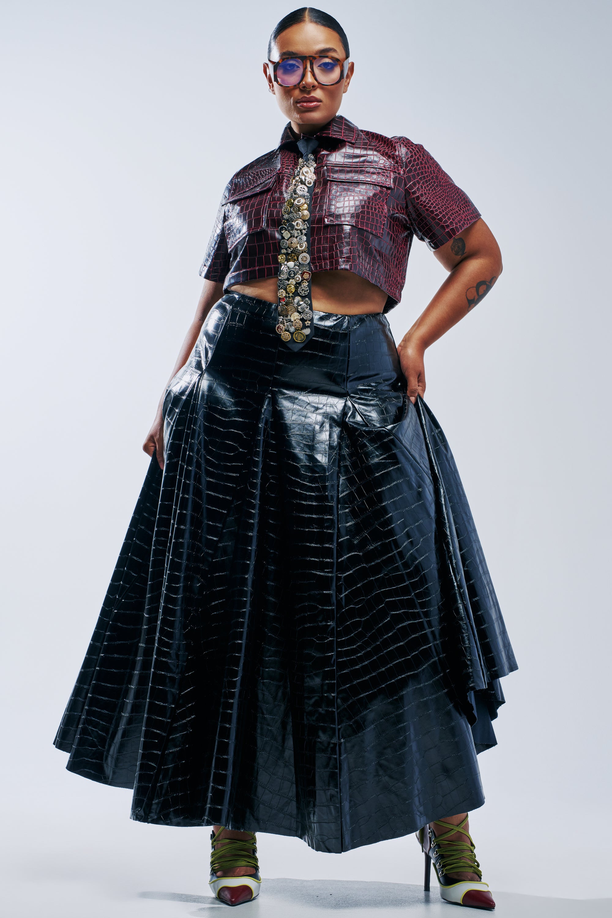 A person wearing a SO CHIC CROC MAXI SKIRT in crocodile-embossed black, a dark red short-sleeved collared shirt, and a long decorative tie.