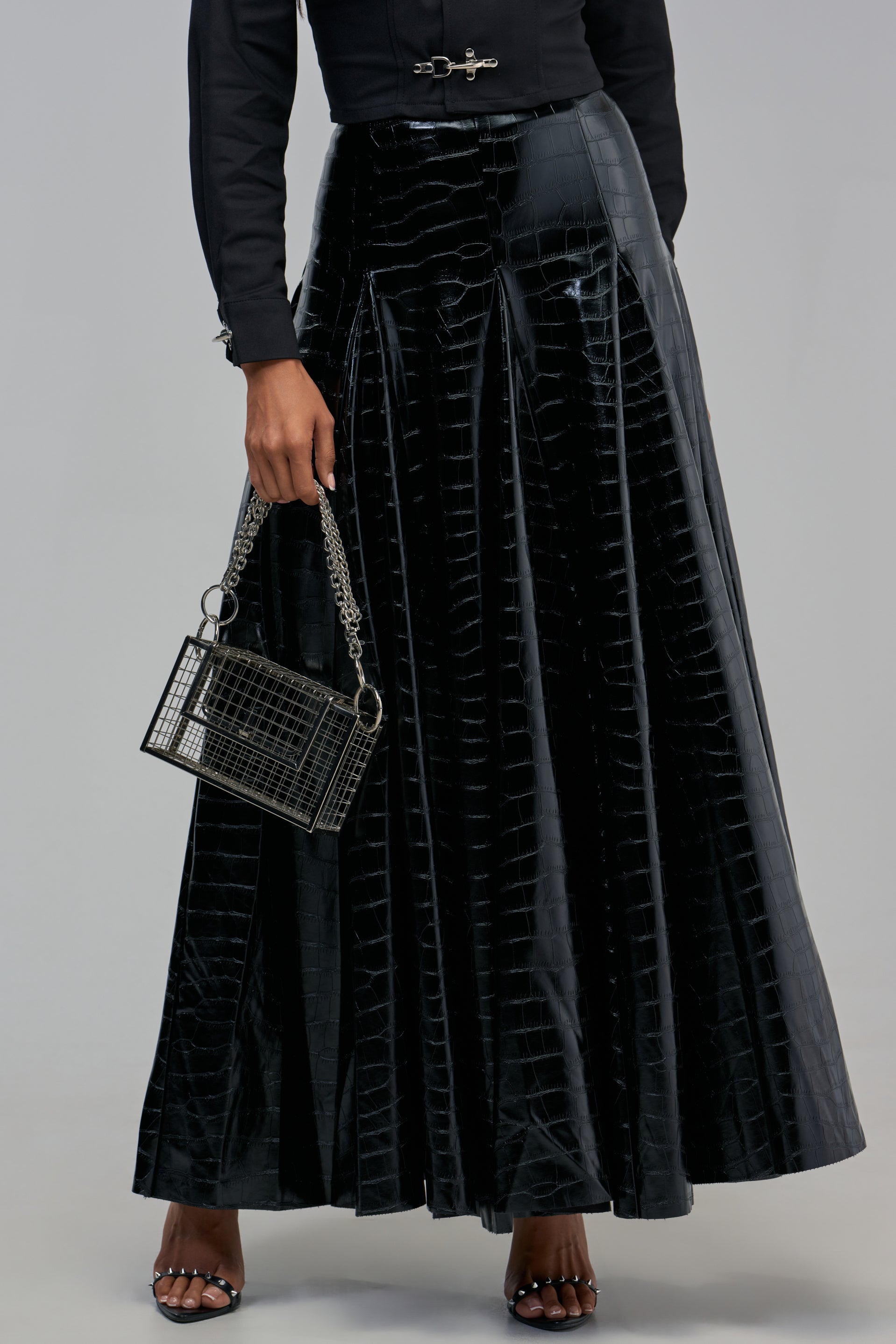 A person wears a black SO CHIC CROC MAXI SKIRT and carries a rectangular, grid-patterned handbag with a chain strap.