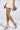 A woman in a gold mini dress and AKIRA SACHITA Silver and Gold Stiletto Sandals stands against a light background, holding a metallic silver clutch. The sandals' faux leather upper and comfort cushion insoles enhance her glamorous look while promising ease with every step.