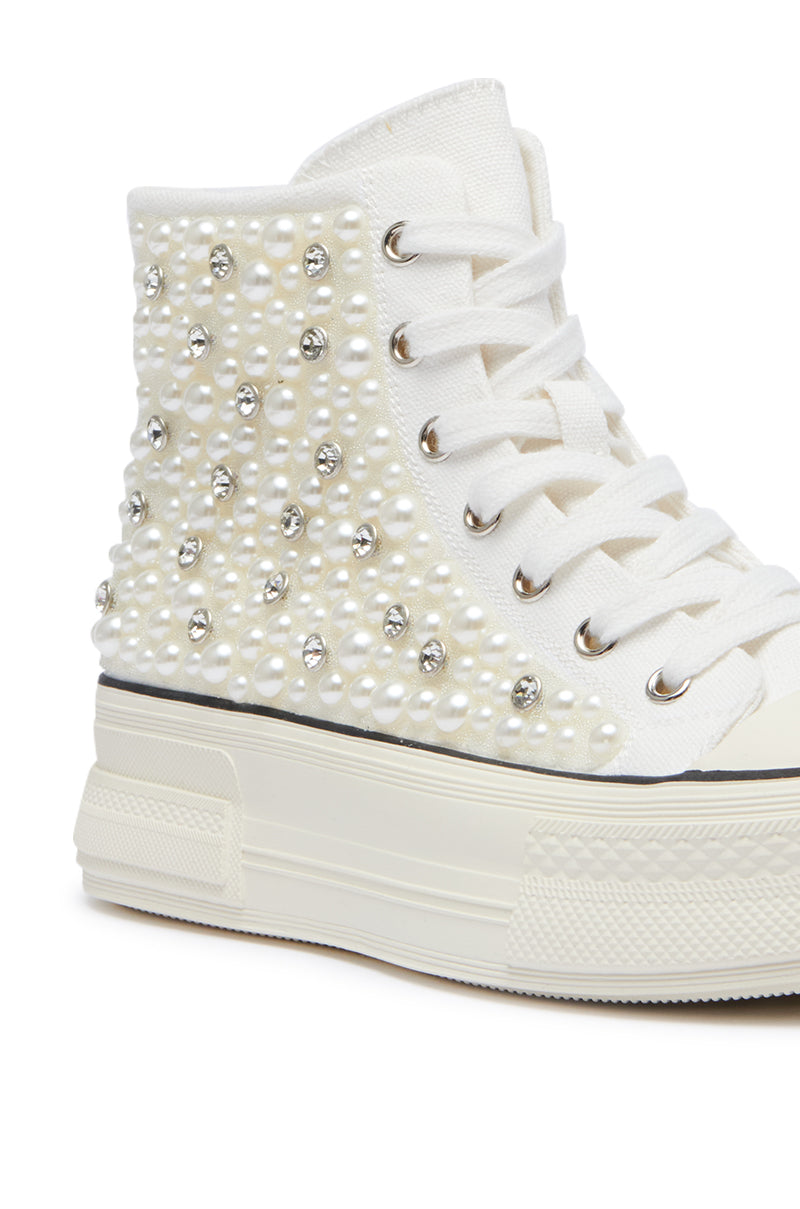 Close-up of the AZALEA WANG SAISHA PEARL WHITE SNEAKER, a high-top design with a thick sole, adorned with small pearls and crystal-like studs on the sides. The sneaker features white laces threaded through silver eyelets. The textured sole boasts a classic pattern, making these embellished shoes a true statement piece.