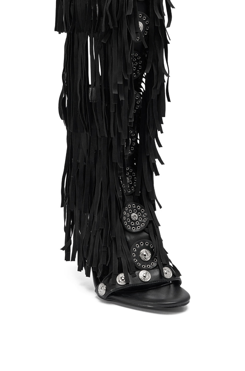 The AZALEA WANG SAMEYANA Black Fringe and Metal Stiletto Gladiator Sandal features a black stiletto heel, long fringe, and silver studs and grommets, shown from the front and slightly angled.