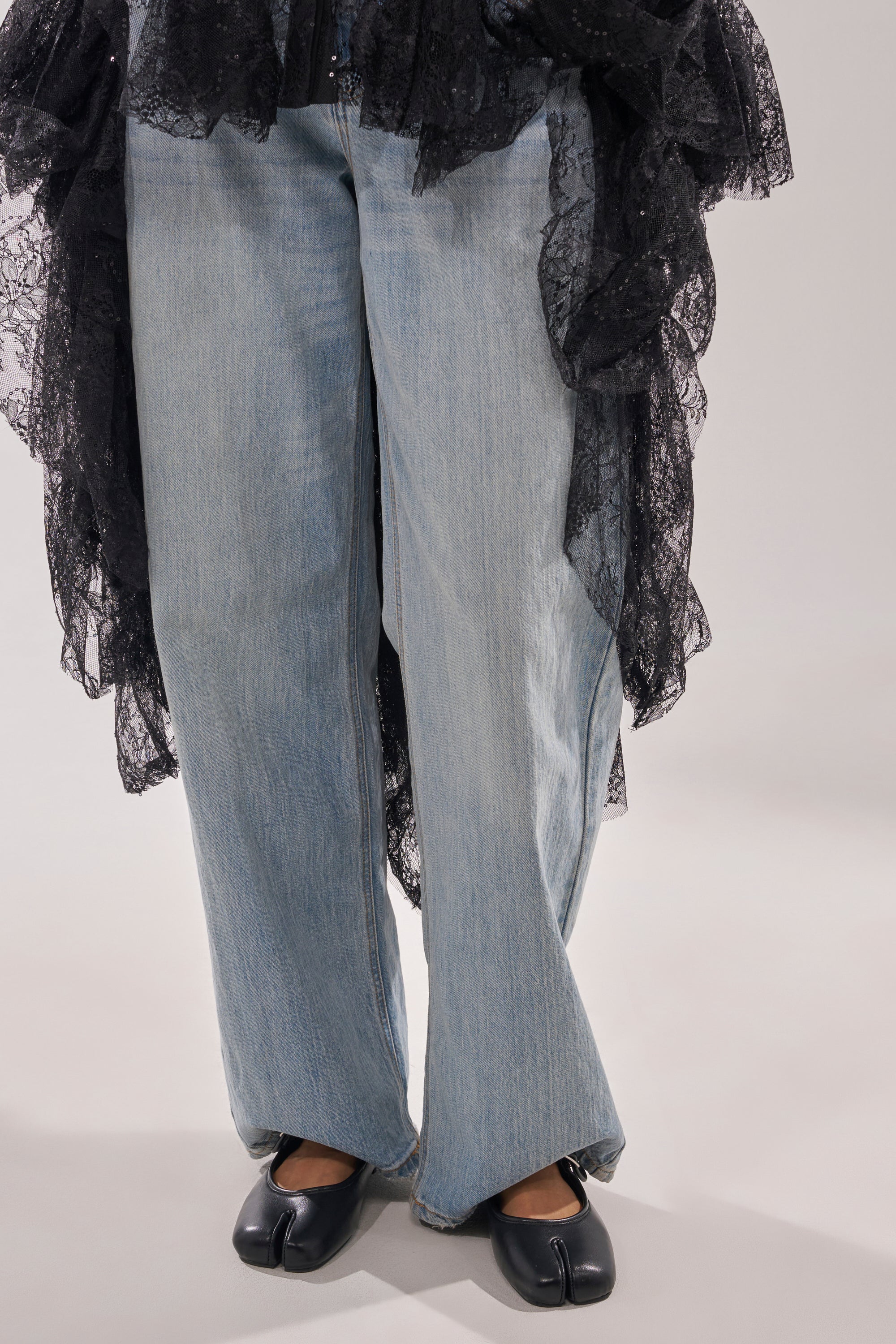 Wearing light blue wide-leg jeans and a flowing black lace garment, the person stands on a light background, paired with AKIRA GOLD SANG BLACK PU SPLIT TOE FLAT shoes featuring a sleek split square toe design. 2