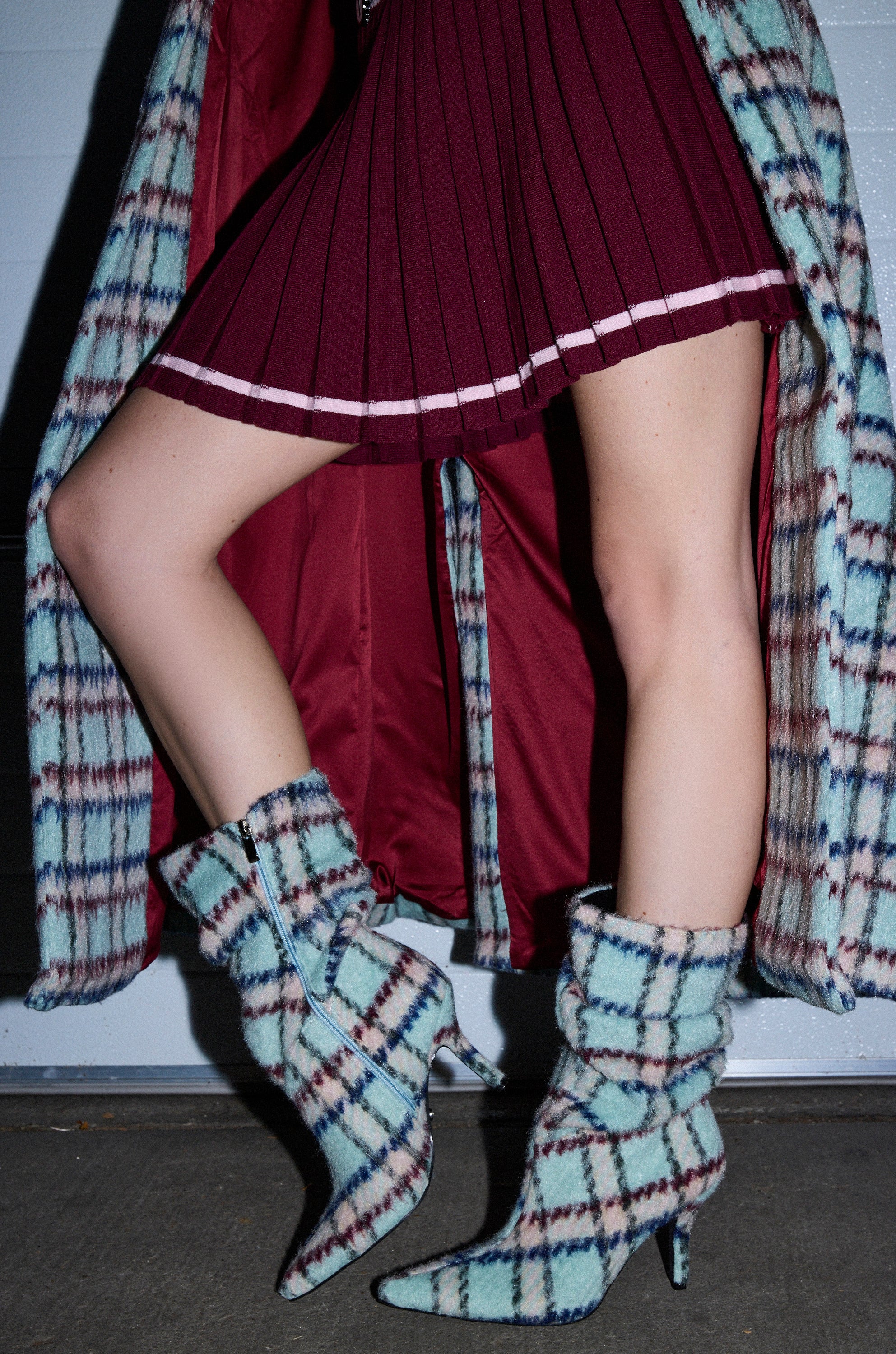 A person poses indoors in a burgundy pleated skirt, matching open coat with burgundy lining, and AZALEA WANG SANJIV BLUE MULTI PLAID STILETTO BOOTIE.