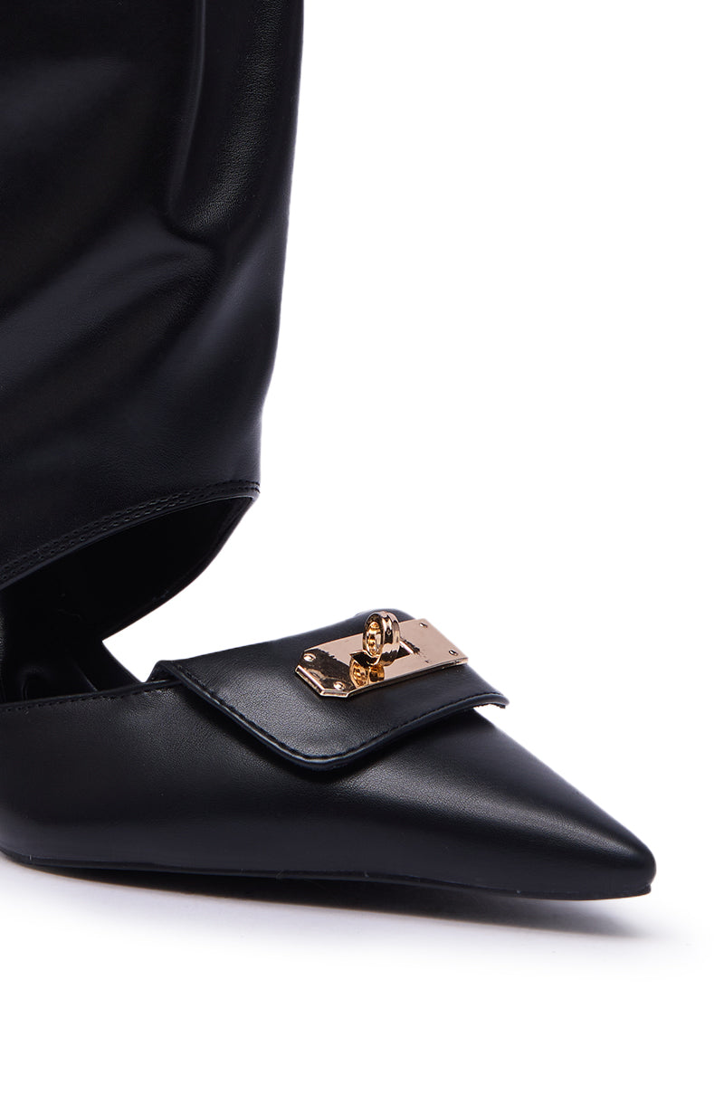 Close-up of the AZALEA WANG SARVESH Black Cutout Stiletto Bootie, featuring a pointed toe, unique flap design, and gold metallic clasp detail on the front, styled with black pants.