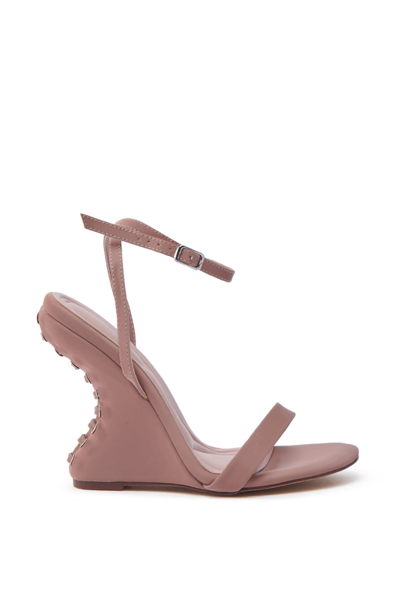 The AZALEA WANG SAWNEY MAUVE LACE UP PATENT SANDAL is a pink high-heeled open-toe shoe, featuring an ankle strap and a faux leather finish. The wedge heel boasts an unusual curved design with a textured back resembling small pegs.