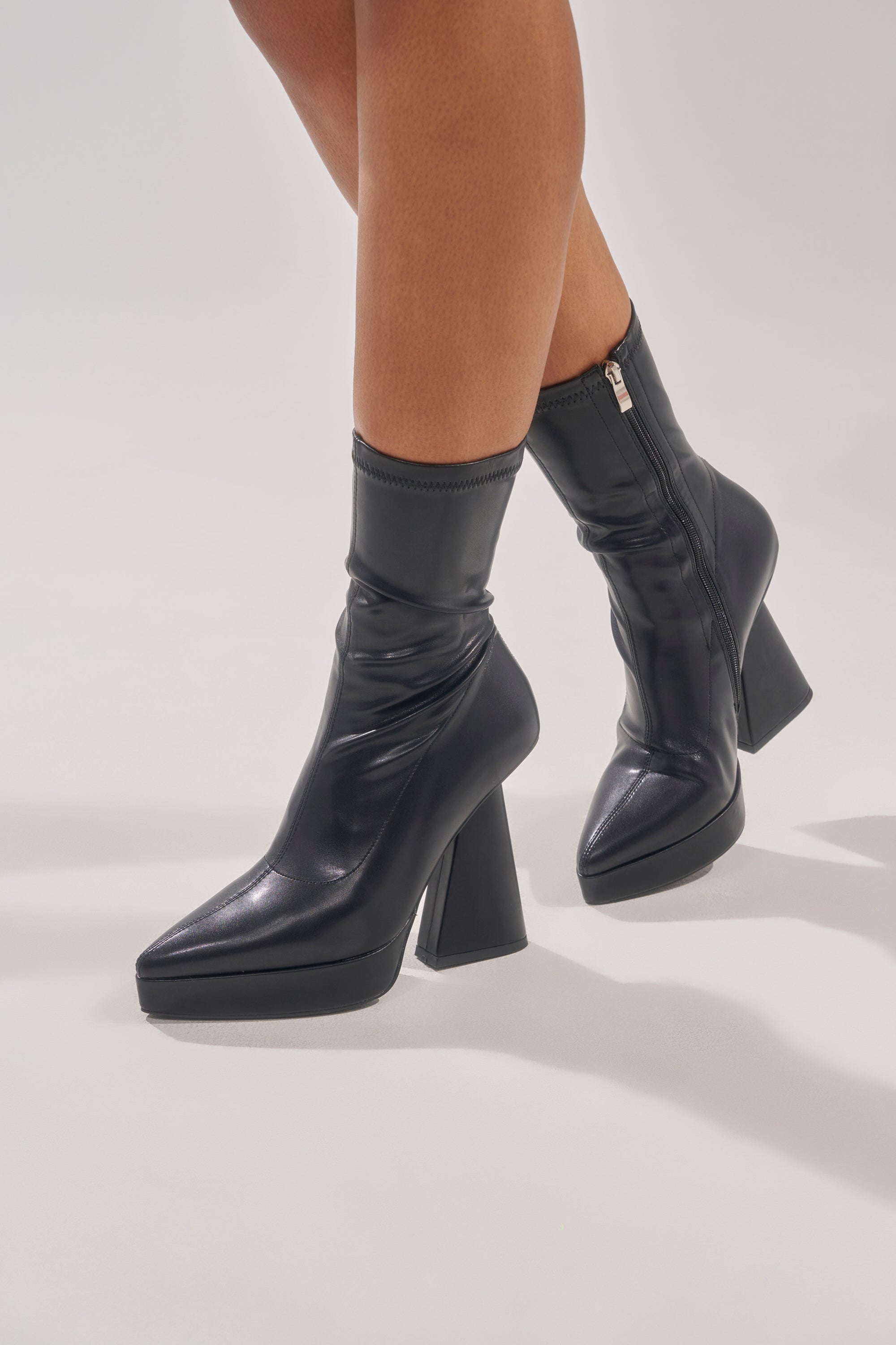 Someone stands on a light gray background wearing the AZALEA WANG SAXTON Black PU Chunky Pointed Toe Bootie with side zippers. 1