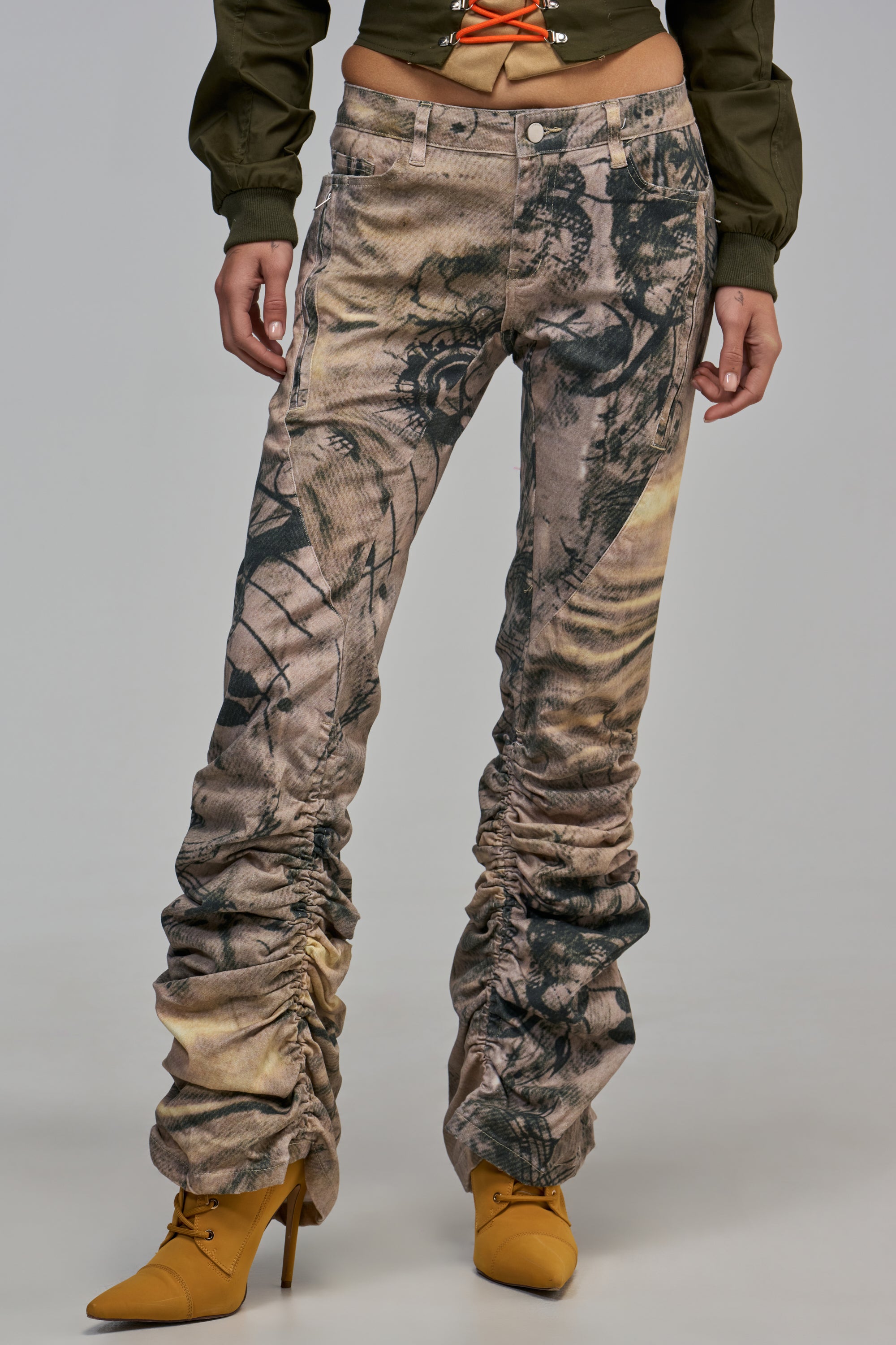 EVIL EYE STACKED DENIM: low-rise, slim-fit abstract print jeans with heavily gathered, stacked fabric at the ankles, paired with mustard yellow heeled booties.