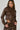 A person with braided hair is wearing the UP TO IT LACE UP MOTO faux leather jacket, featuring decorative stitching and matching pants. They're standing against a plain backdrop, looking slightly to the side, highlighting a trendy cropped silhouette.