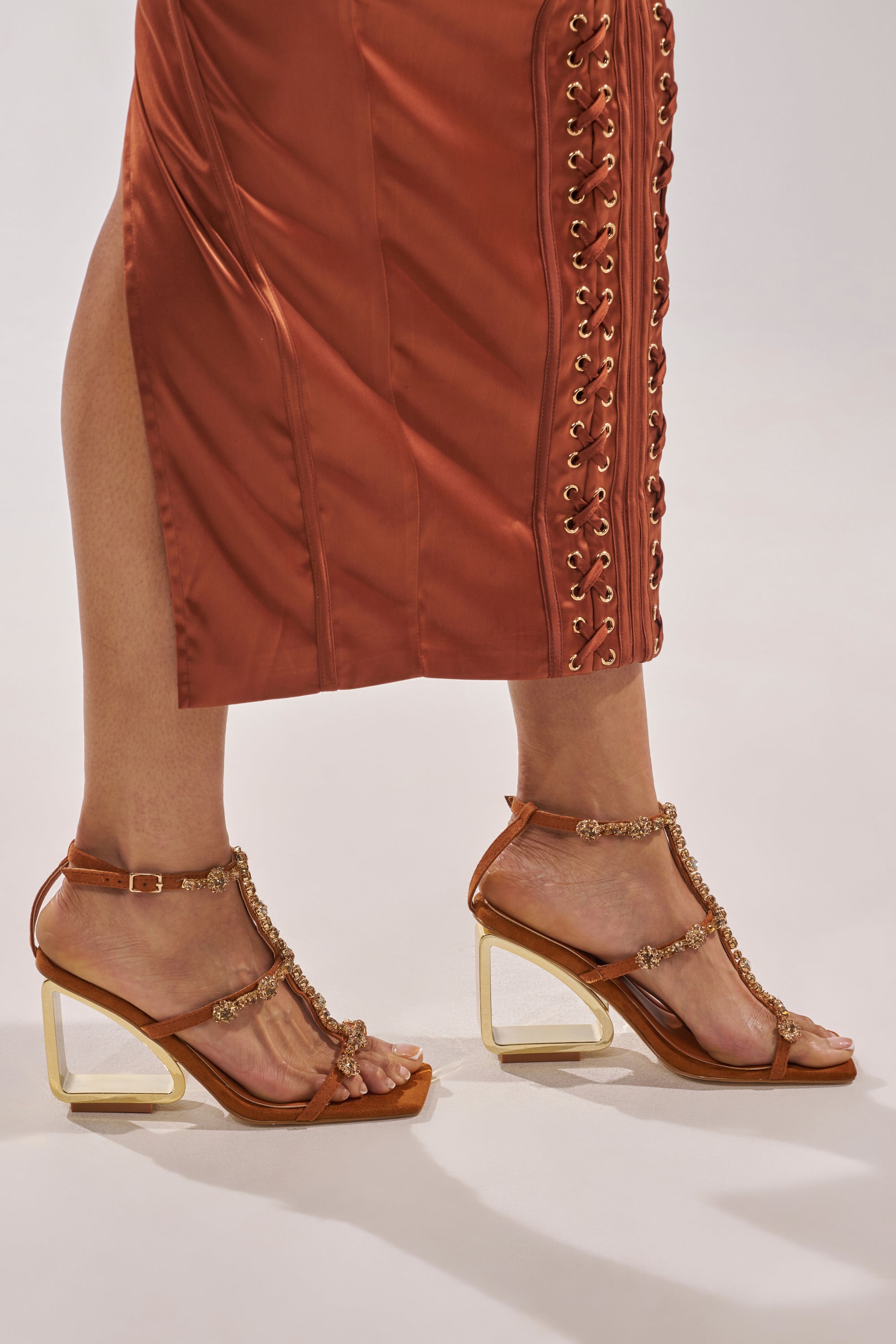 A person in rust-colored lace-up pants and AZALEA WANG SCHANTELLE Tan Embellished Upper Wedge Sandals with gold accents and a comfort cushion insole, standing against a light background. 1