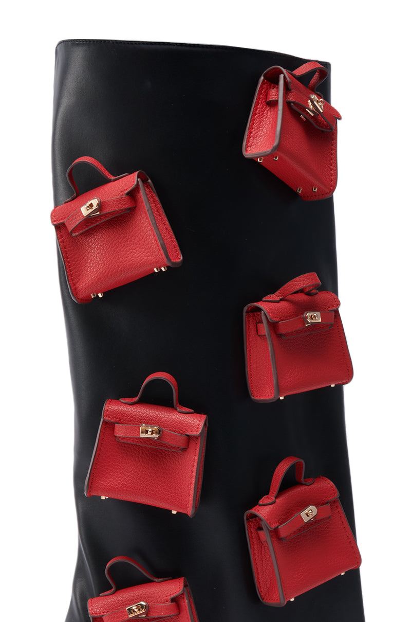A close-up of the AZALEA WANG SCIPIO BLACK PURSE BOOT, a black faux leather boot adorned with multiple small red handbag-shaped accents.
