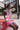 A woman in the WILD THANG PRINTED MINI DRESS with a bold zebra and pink floral print plus a wide gold belt sits on a red picnic bench. Behind her, a mural reads “WE BUILT Gold! SINCE 1969” with an arrow pointing right.