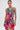 A woman models the WILD THANG PRINTED MINI DRESS, featuring a sleeveless zebra print with bold pink tropical flowers, against a plain white background. Her hair is tied back and she wears large hoop earrings.