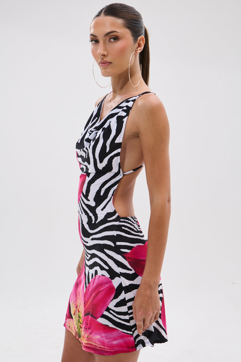 Model wears the WILD THANG PRINTED MINI DRESS, a sleeveless zebra print mini dress with vibrant tropical flowers, a large pink floral design, and side cutout, set against a plain white background. 5
