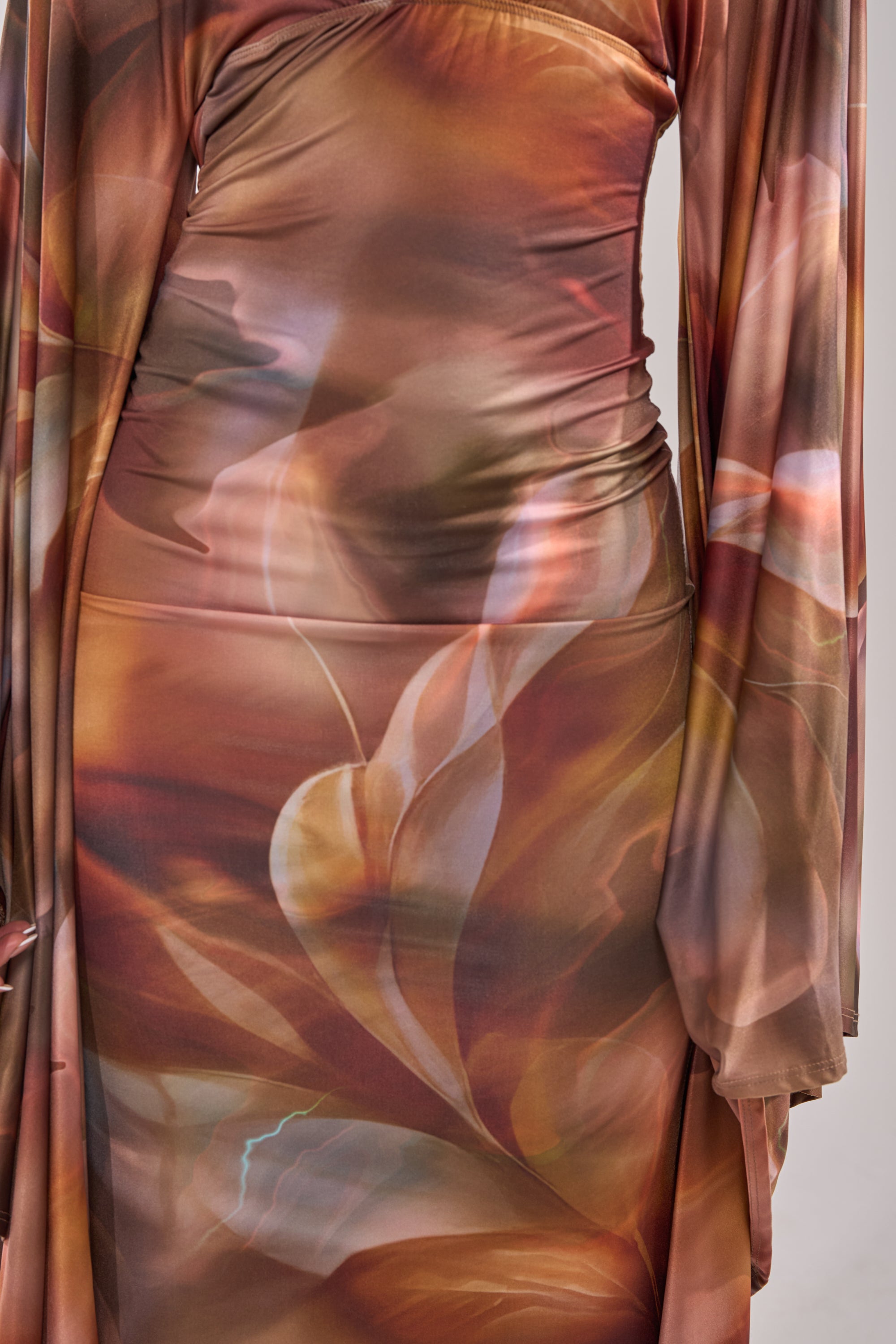 A close-up of the SHINY LIKE ME MAXI DRESS highlights its long sleeves, body-skimming silhouette, and a flowing abstract floral pattern in earthy brown, orange, and beige tones. 7