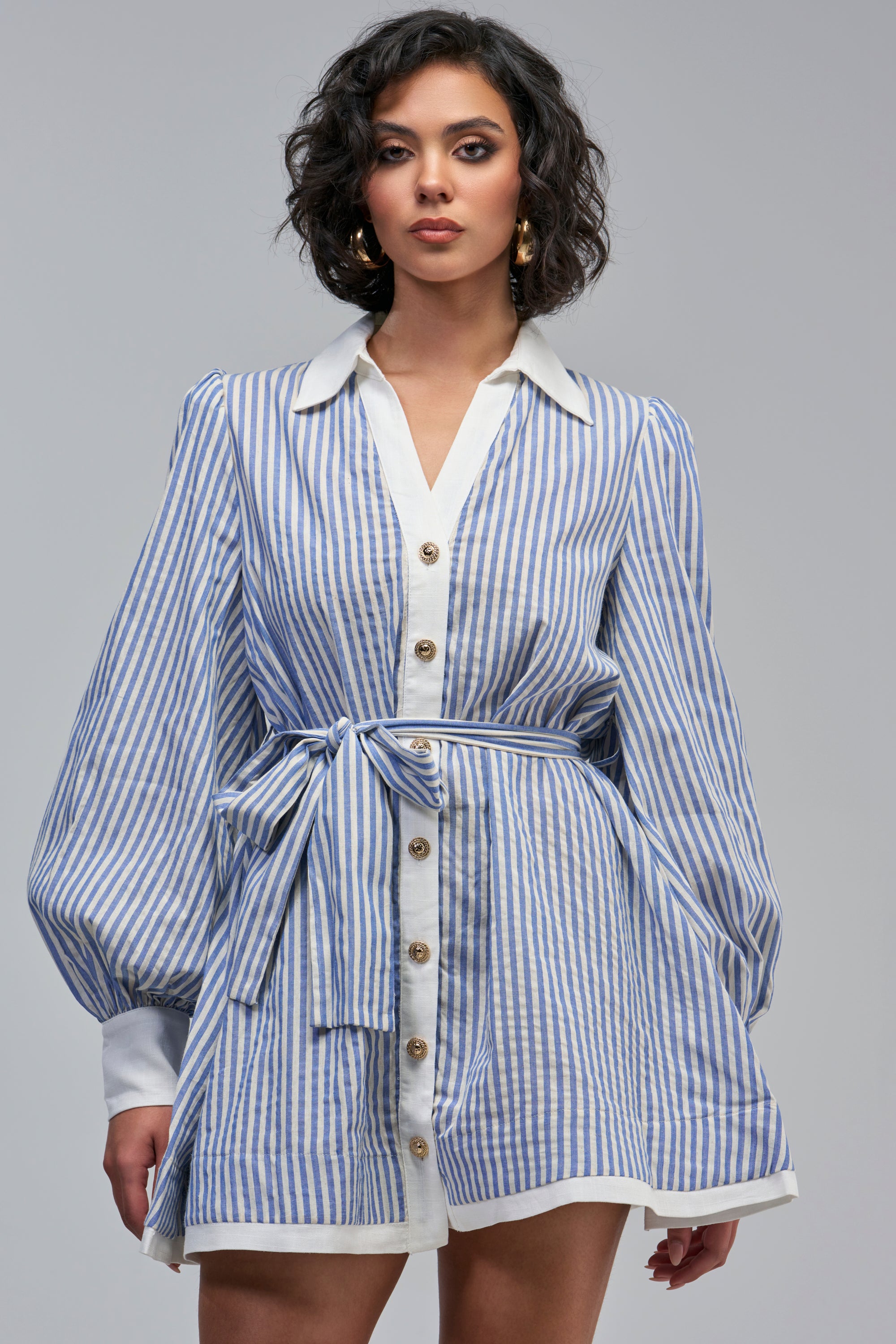 The COUNTRY CLUB STRIPED MINI DRESS is a blue and white striped linen mini dress featuring a white collar, button-front closure, balloon sleeves, and a matching fabric tie at the waist.
