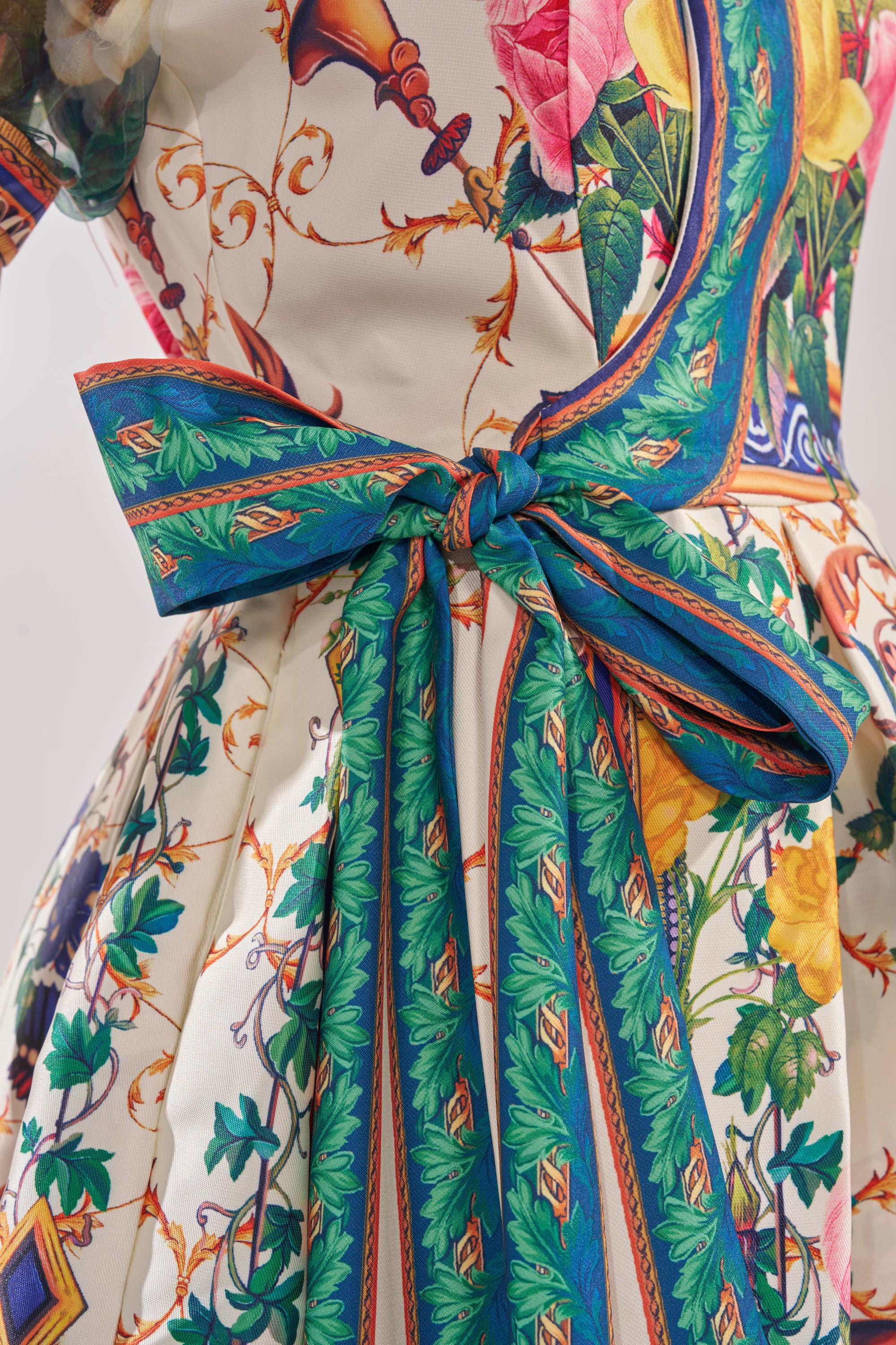 Close-up of the FLOWER GIRL SATIN MAXI DRESS, a floral wrap maxi with a green and blue sash bow, featuring vivid botanical prints and decorative detailing. 6