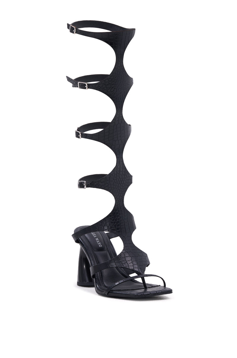 The AZALEA WANG SEAMUS BLACK CROC NOVELTY HEEL SANDAL is a black gladiator-style sandal with an open toe, sculpted chunky heel, croc-embossed texture, wavy cut-out straps, and five adjustable buckles up to the knee.