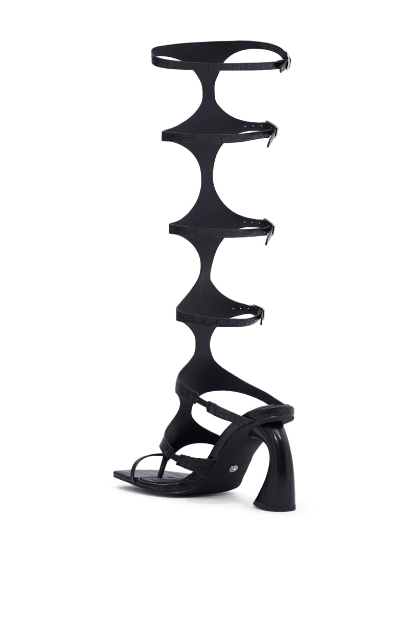 Make a statement in the AZALEA WANG SEAMUS BLACK CROC NOVELTY HEEL SANDAL, featuring four wide, curved straps with buckles up to the knee and a bold sculpted chunky heel for an unforgettable gladiator-inspired look.