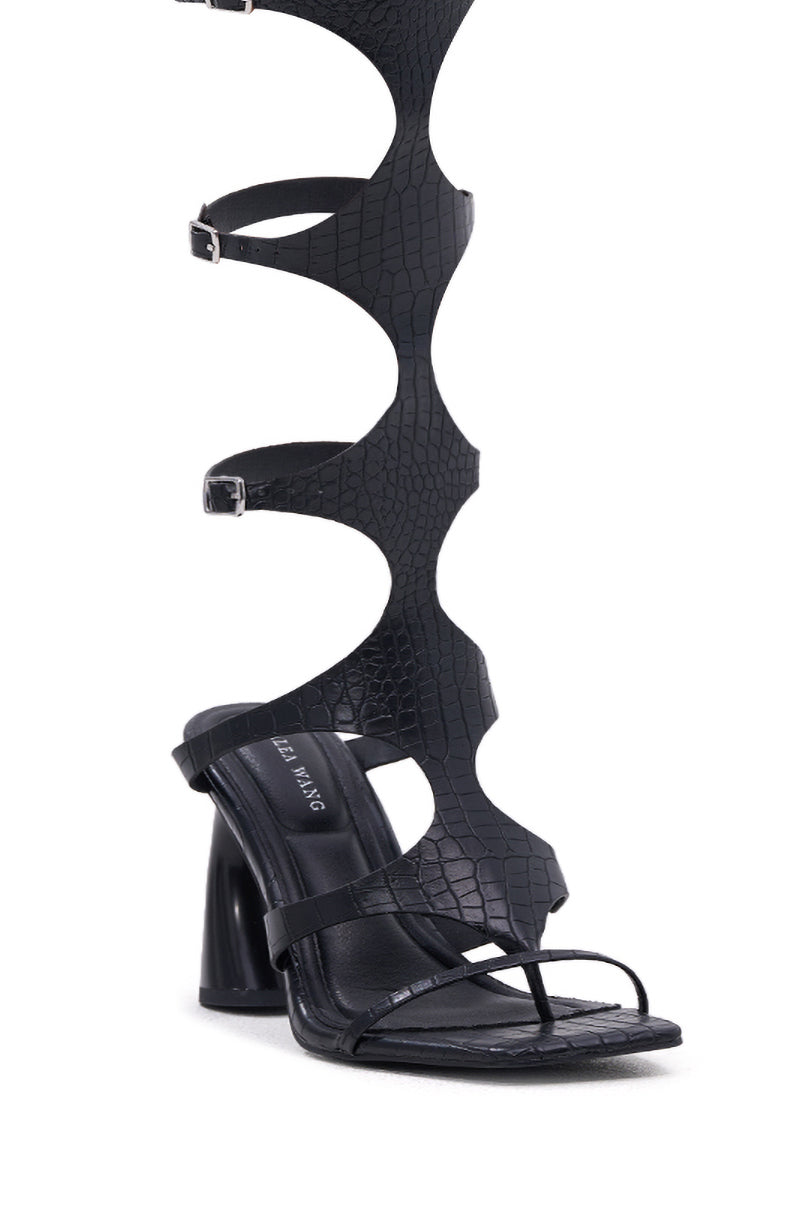 The AZALEA WANG SEAMUS BLACK CROC NOVELTY HEEL SANDAL features a bold gladiator style with knee-high wavy straps, multiple buckles, and a sculpted chunky heel in a black croc finish.