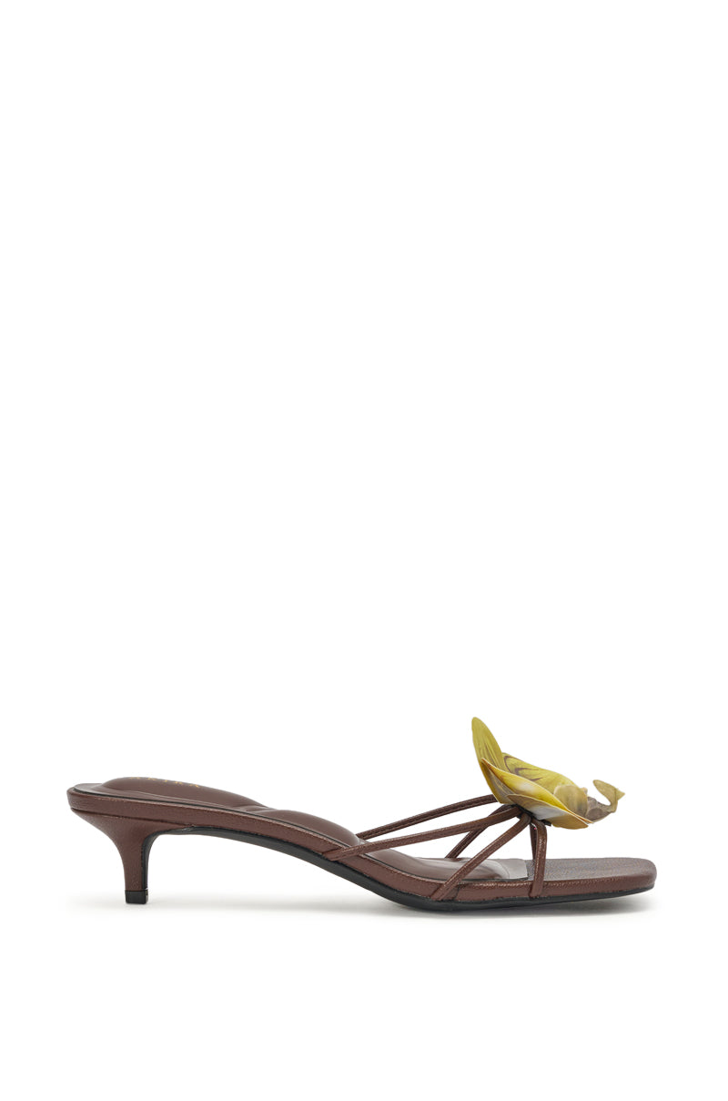 The AKIRA SELA CHOCOLATE SLIP ON FLOWER SANDAL is a chic faux leather brown sandal with thin straps, a kitten heel, and a yellow floral accent on the front—perfect summer resort footwear, pictured in side profile against a white background. 2