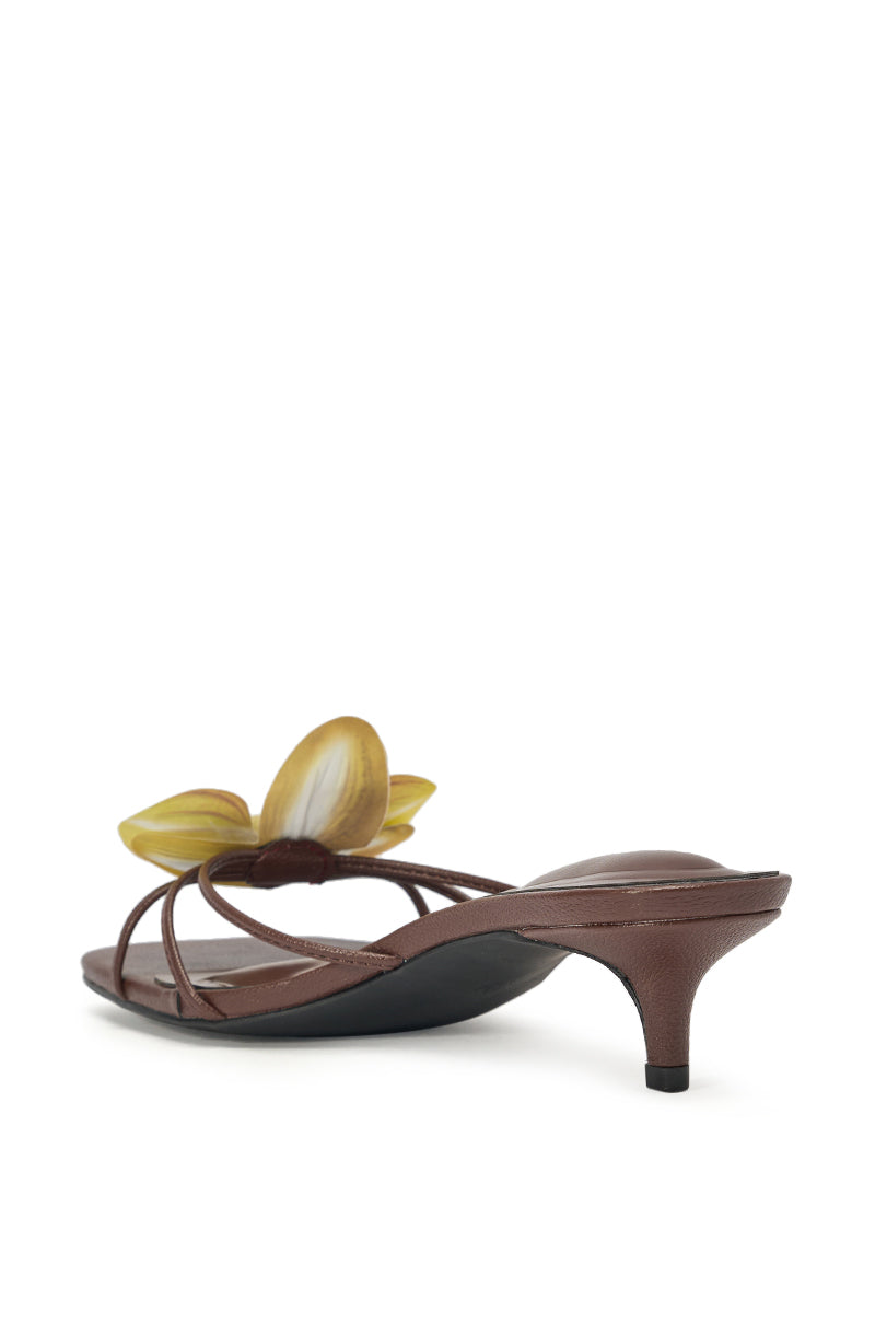 The AKIRA SELA CHOCOLATE SLIP ON FLOWER SANDAL is a brown faux leather kitten heel with thin straps and a bold yellow flower accent, showcased at an angle to highlight its chic side and back design. 4