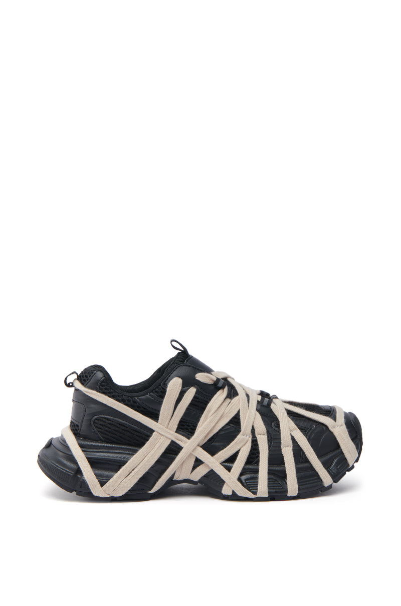 The AZALEA WANG SELIE BLACK LACE UP SNEAKER features chunky soles, a performance-inspired silhouette, and bold beige laces that criss-cross for a unique web-like streetwear look. Shown in black, side view on white background.