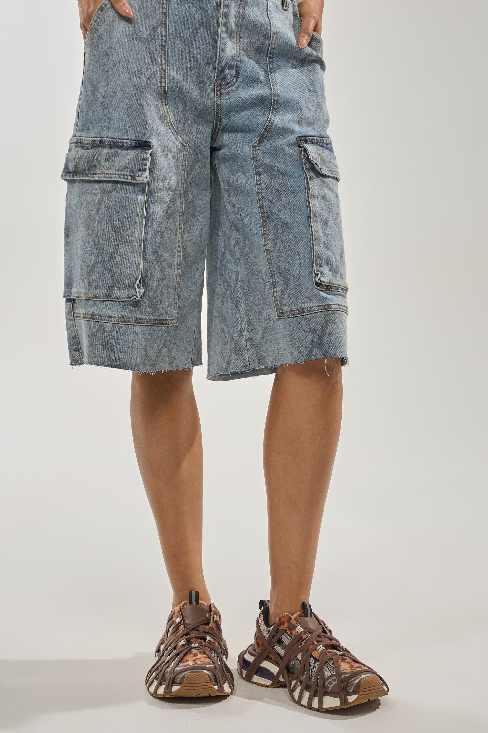 A person wearing knee-length, light blue, patterned denim cargo shorts with frayed hems and AZALEA WANG SELIE LEOPARD PRINT LACE UP SNEAKERS stands against a plain light background. 1