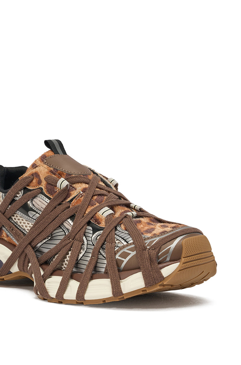 A close-up of the AZALEA WANG SELIE LEOPARD PRINT LACE UP SNEAKER, featuring a brown and tan leopard print, crisscrossing brown straps, lace detail, white accents, and a textured tan rubber sole. 5