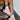 A person sits on the stairs, sporting striped socks and colorful AZALEA WANG SELIE RED FLAT SNEAKERS with a unique textile upper. The backdrop showcases a textured metal step against a white brick wall, highlighting the playful footwear design.