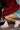 A person sits on stairs, cloaked in a vibrant red and black fur coat, a green dress, and striped socks, paired with the AZALEA WANG SELIE RED FLAT SNEAKER that boasts a textile upper. Their face remains hidden as they blend seamlessly into the industrial setting.