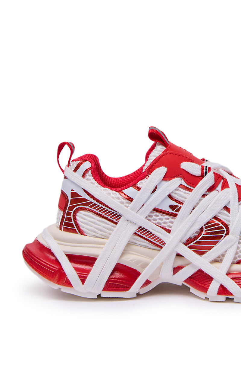 The AZALEA WANG SELIE RED FLAT SNEAKER is a red and white slip-on with overlapping white straps, an intricate design, and a chunky sole, displayed side view on a white background.