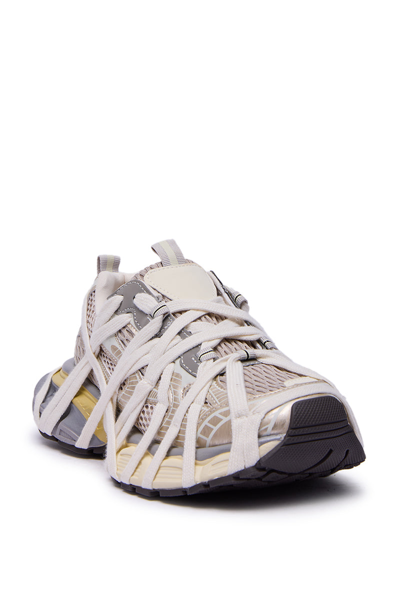 The AZALEA WANG SELIE white flat sneaker features a beige and gray mesh upper with crisscrossed straps, a thick cushioned sole, and a rounded black toe cap, shown from the front angle.